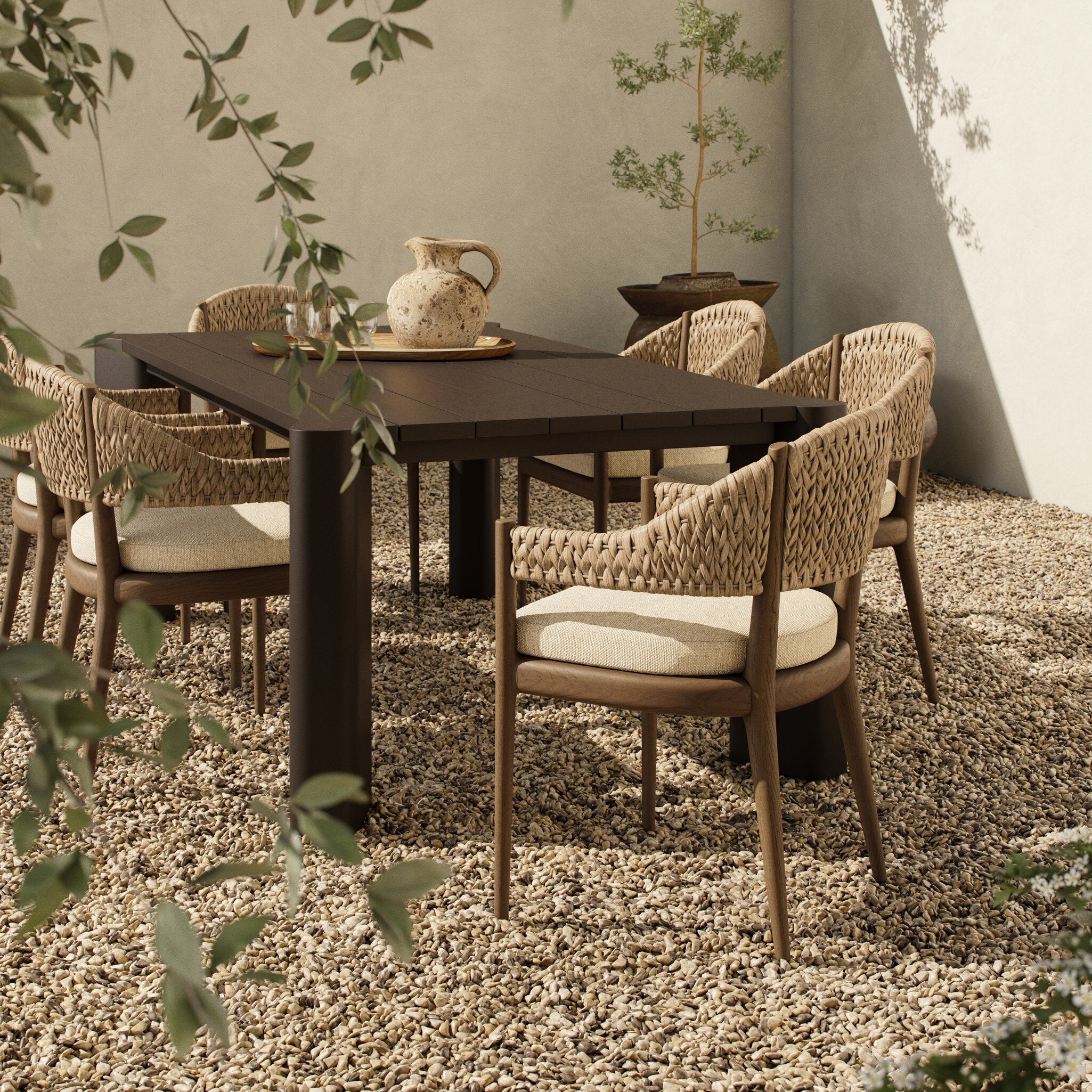 Dining table with wicker chairs on a gravel surface with plants around