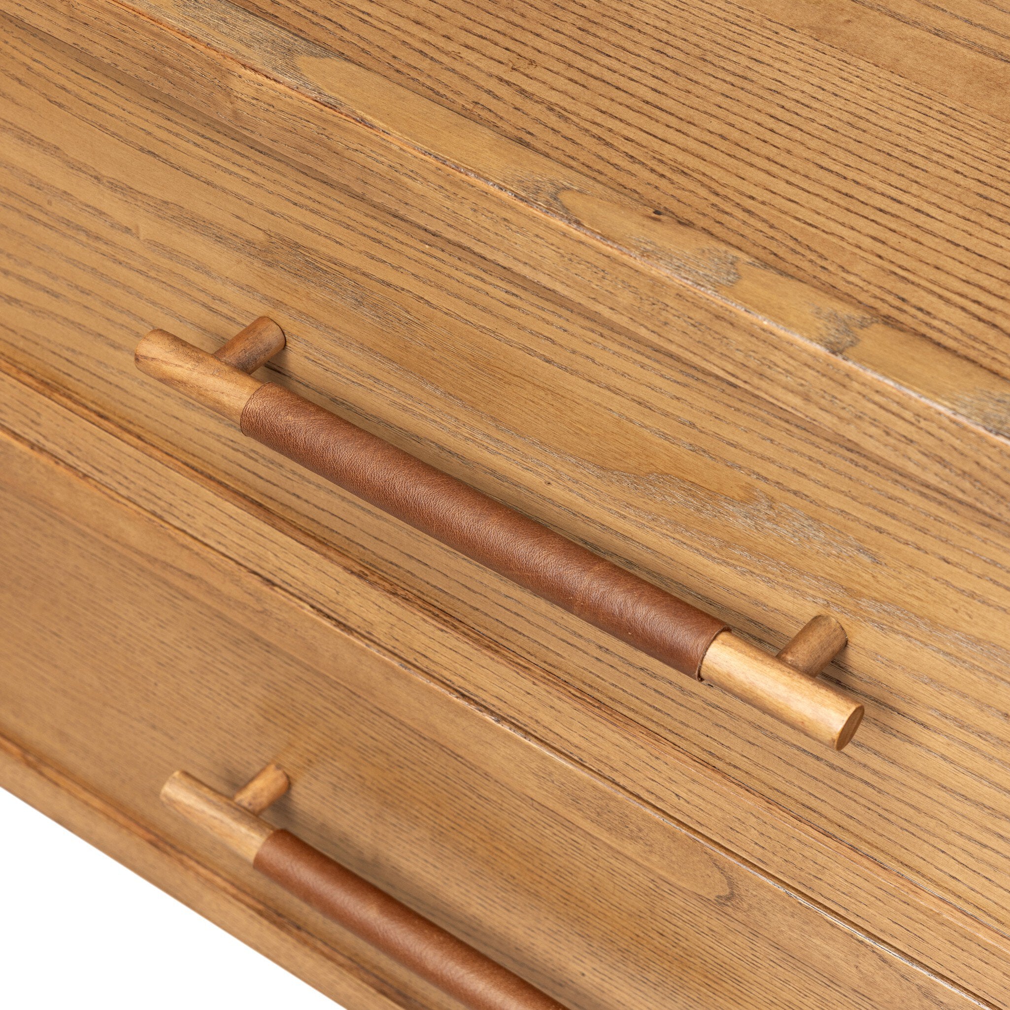 Close-up of a wooden drawer front with two long pull handles wrapped in brown leather and finished with light wood ends, set against a matching wood grain surface.