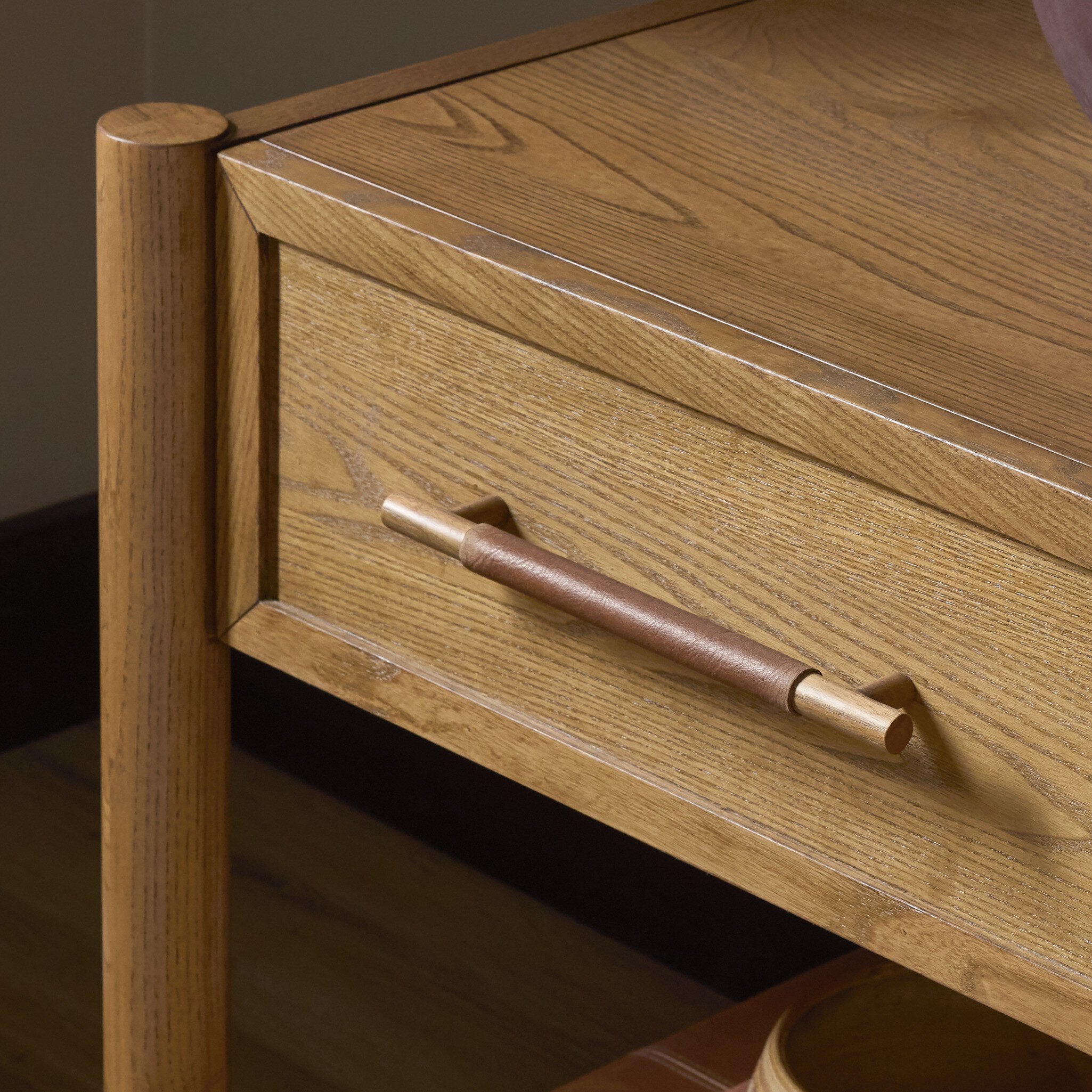 Close-up of a wooden desk or cabinet drawer with a medium brown leather-wrapped pull handle and matching wood grain finish.