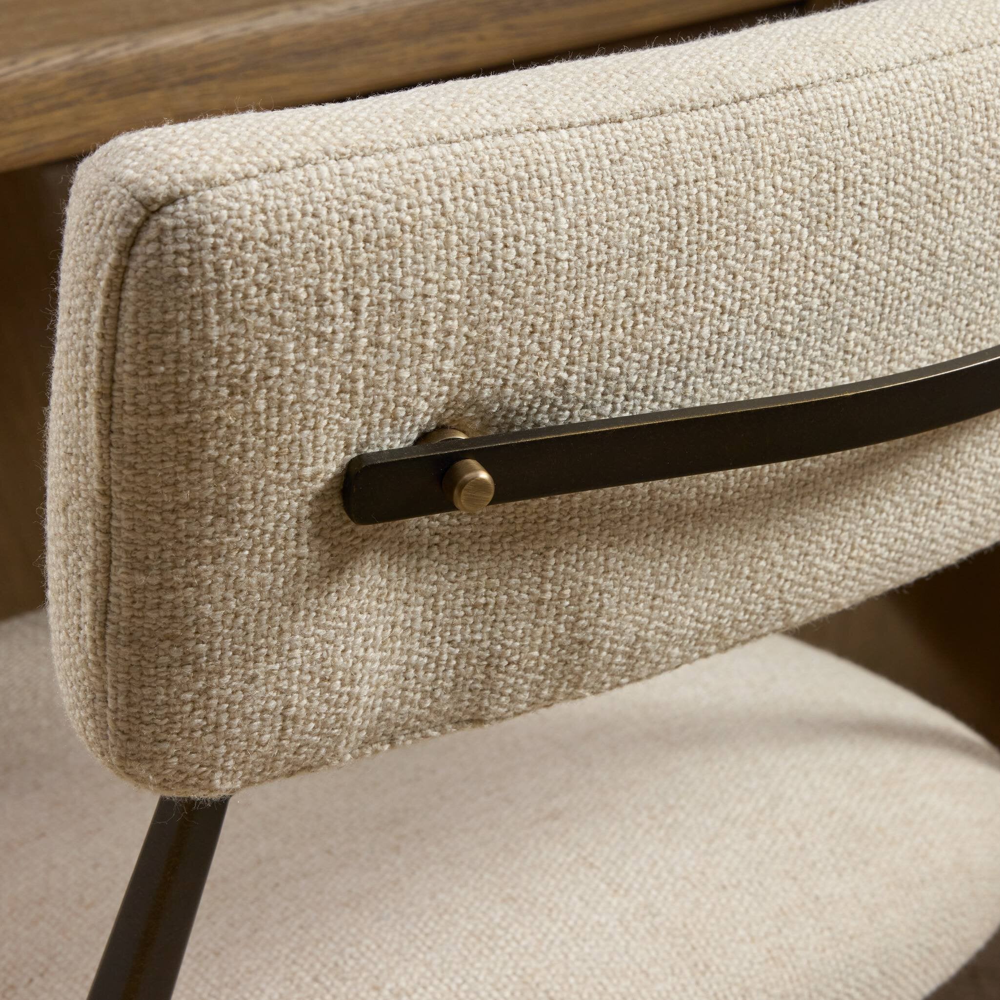 Close-up of a beige upholstered chair with a metal armrest and wooden backrest.