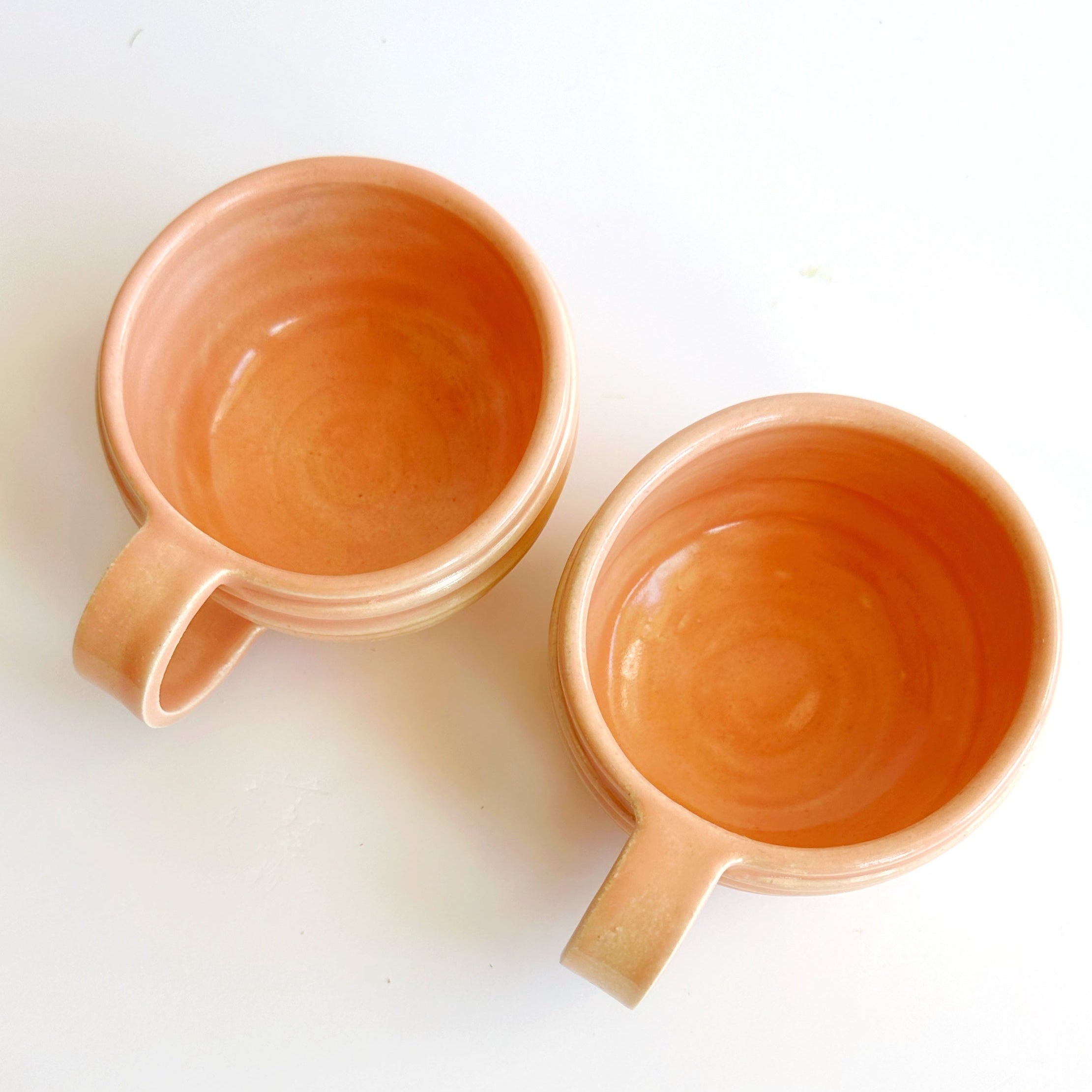 Two peach-colored ceramic mugs on a white background