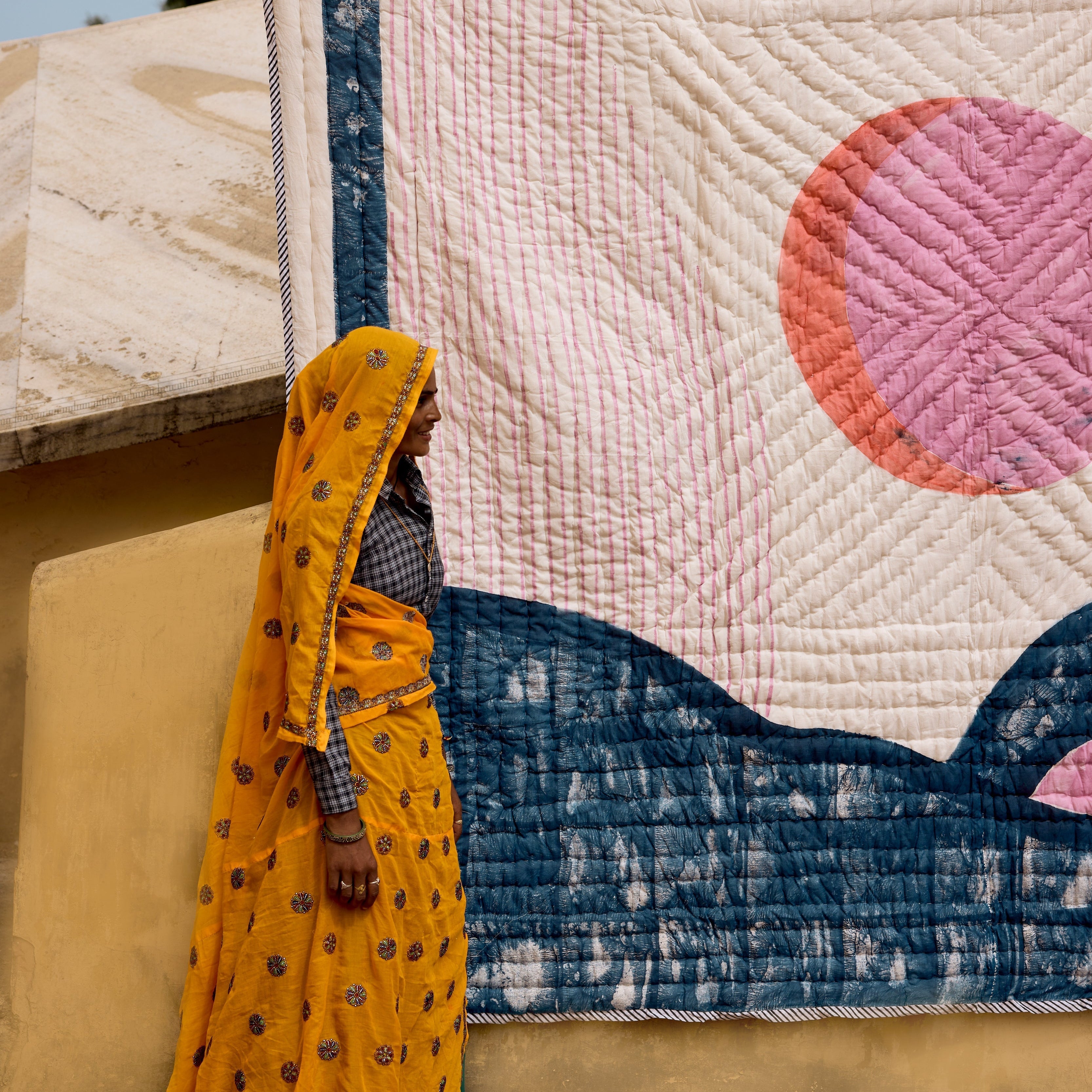 Woman in a yellow saree holding a quilt with a pink circle design.