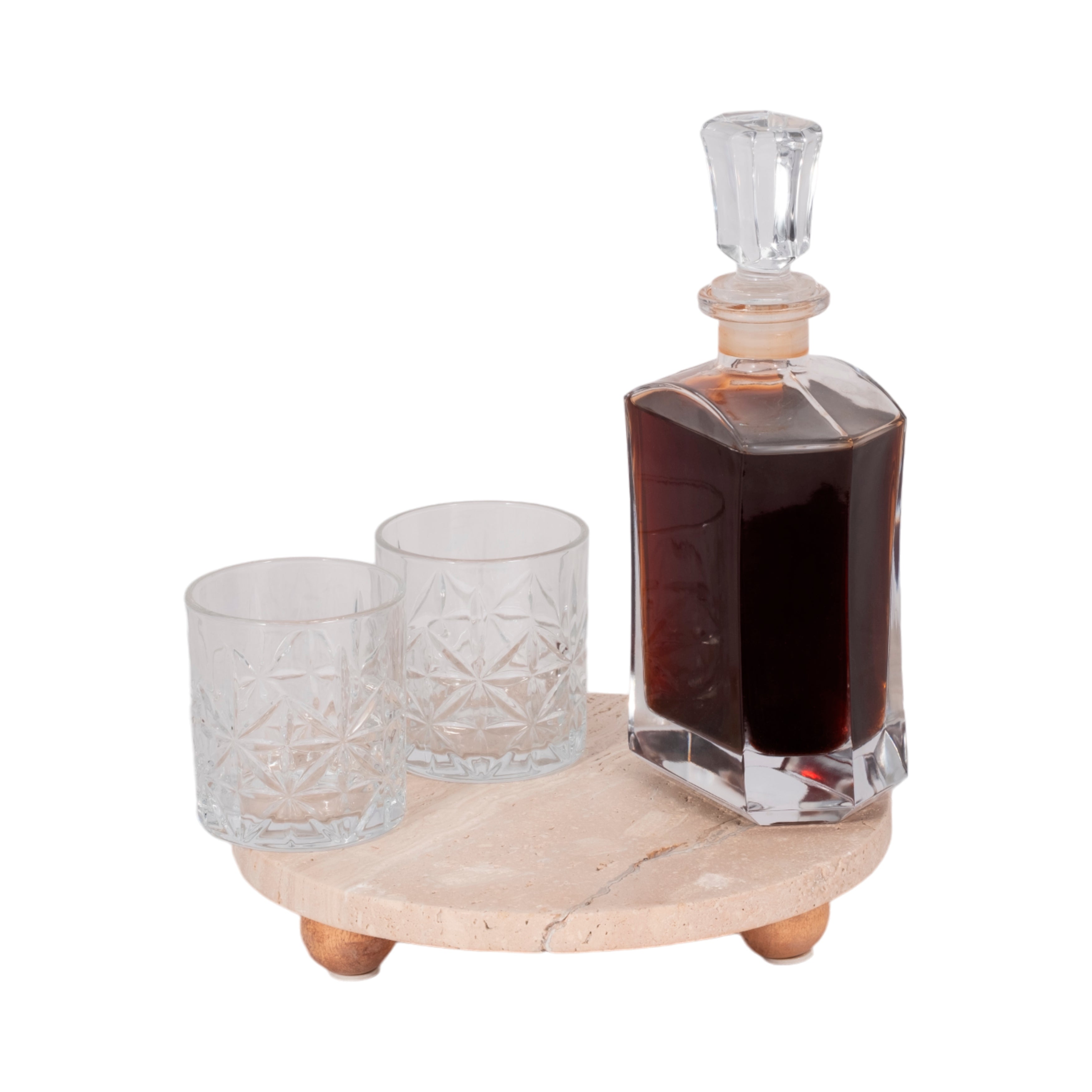Crystal decanter with dark liquid and two glasses on a stone coaster against a white background