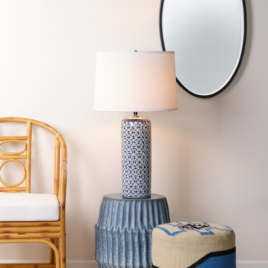 Decorative lamp on a textured side table with a chair and mirror in the background.