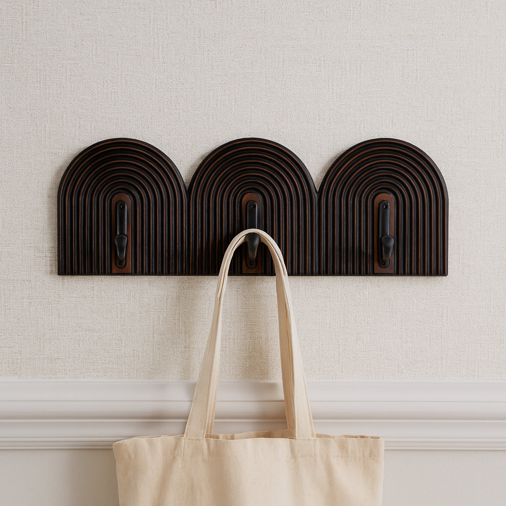 Set of three dark brown wall hooks with a beige tote bag hanging on one of them against a light gray wall.