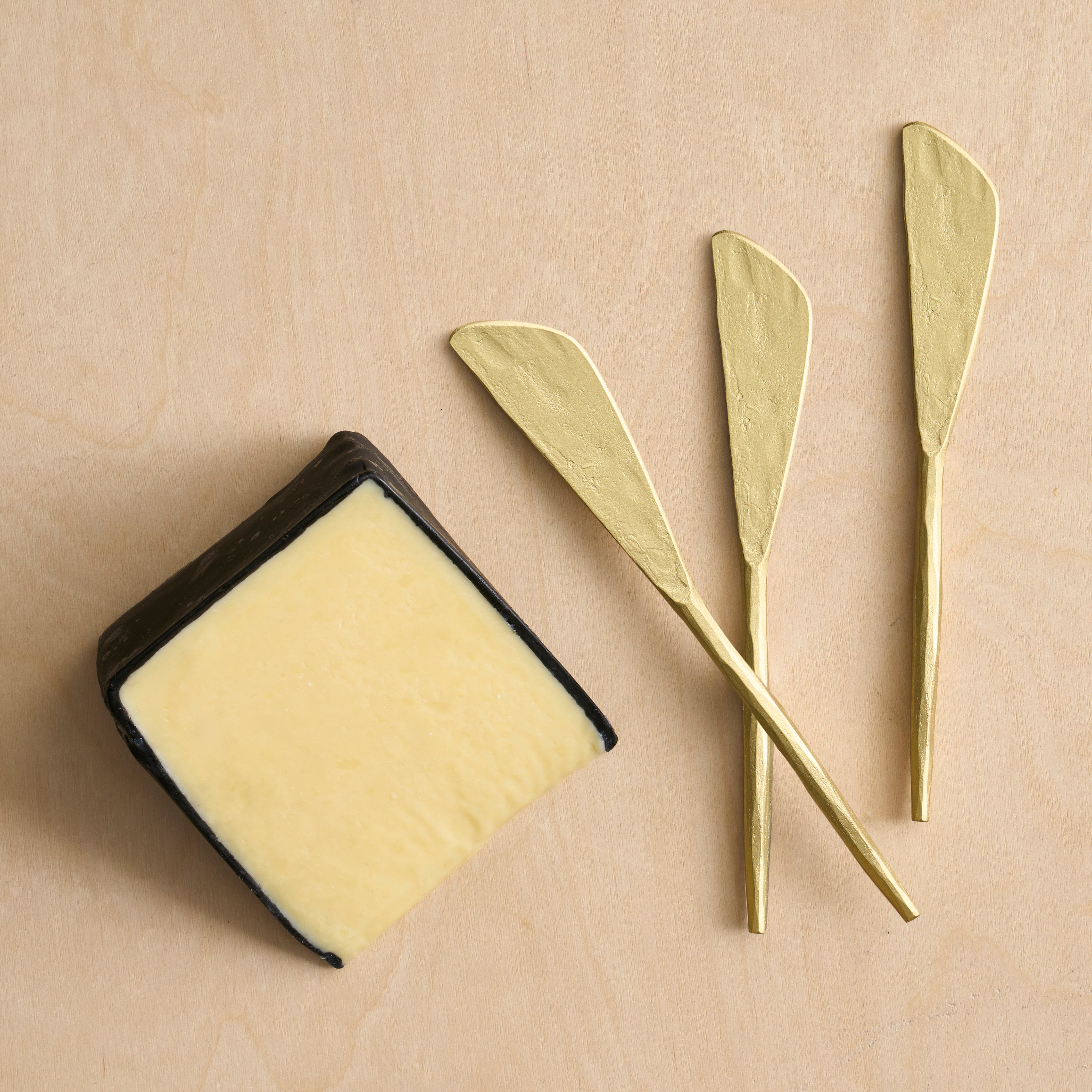 Block of cheese with three gold butter knives on a beige background