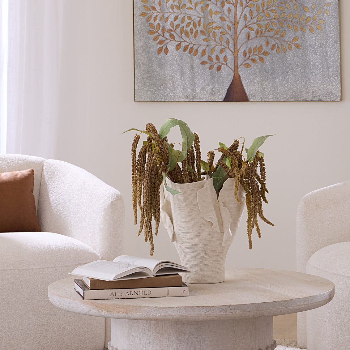 Living room with a round coffee table featuring a vase with plants, books, and an open book.