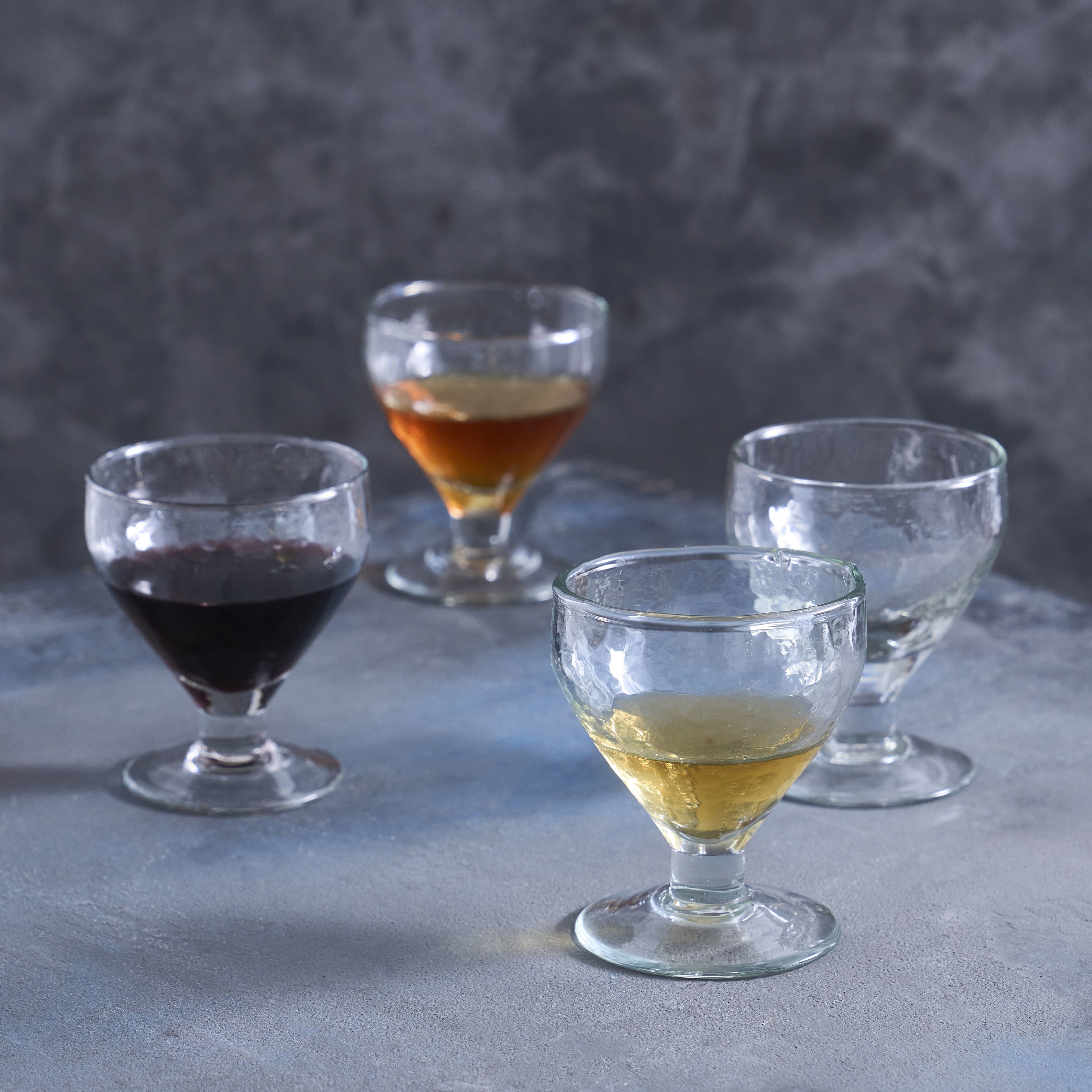 Four glass cups with different liquids on a gray surface and background