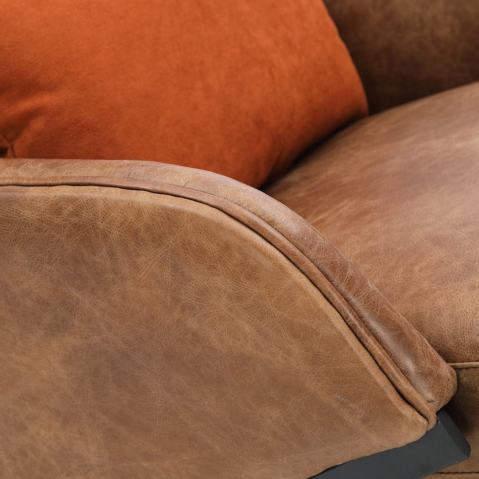 Brown leather sofa with a single orange cushion on a white background
