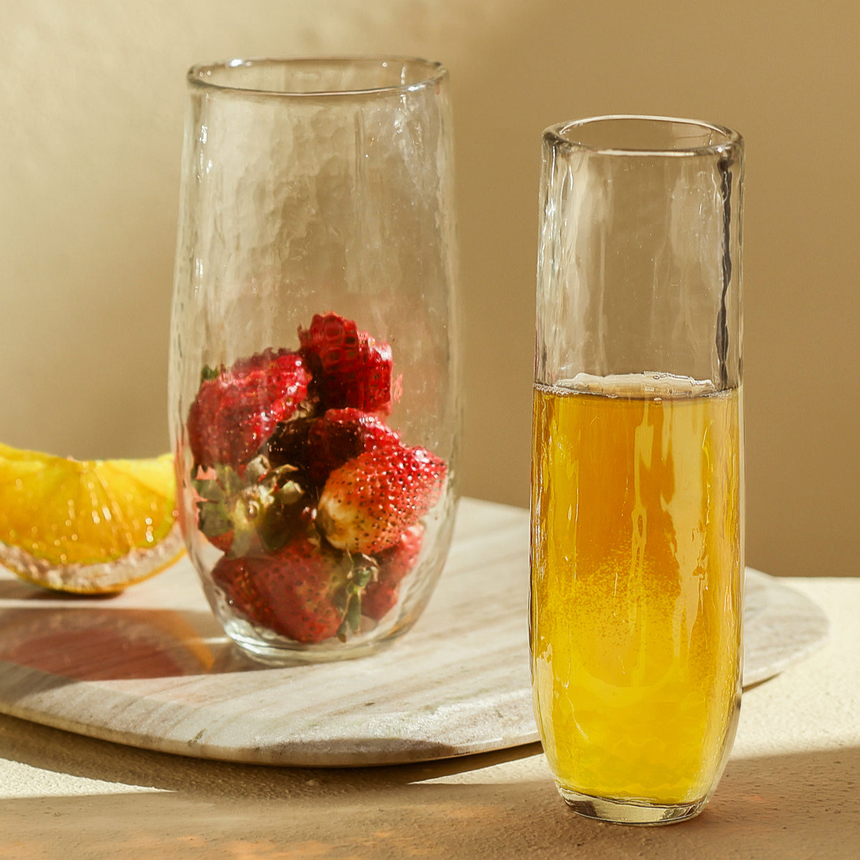 Two glasses, one with strawberries and the other with a yellow liquid, on a wooden surface.