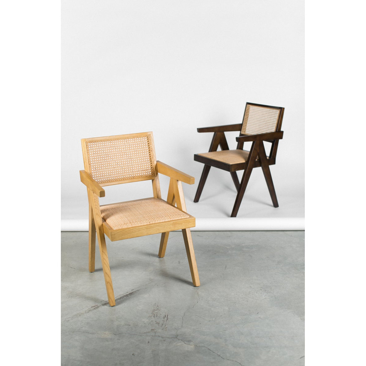 Two chairs, one wooden and one with woven backrest, on a gray floor with a white wall background.