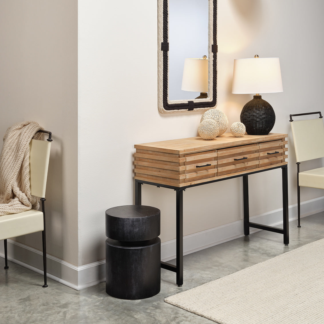 Wooden console table with black legs in a room setting with chairs and decor.