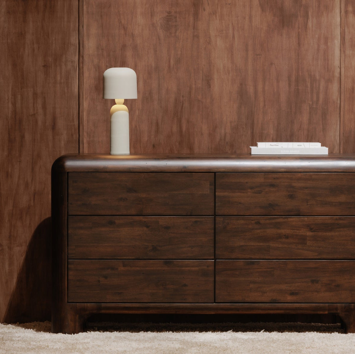 Wooden dresser with a lamp against a wooden wall
