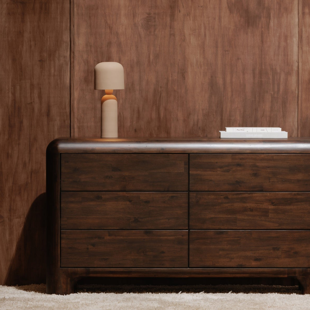 Wooden dresser with a lamp against a wooden wall