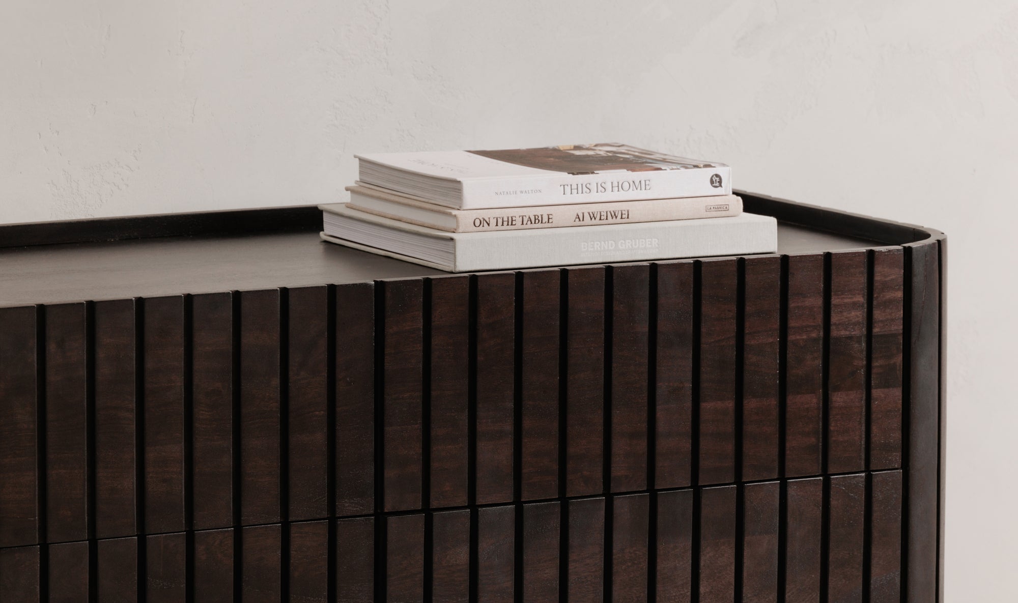 Stack of books on a wooden sideboard against a plain wall