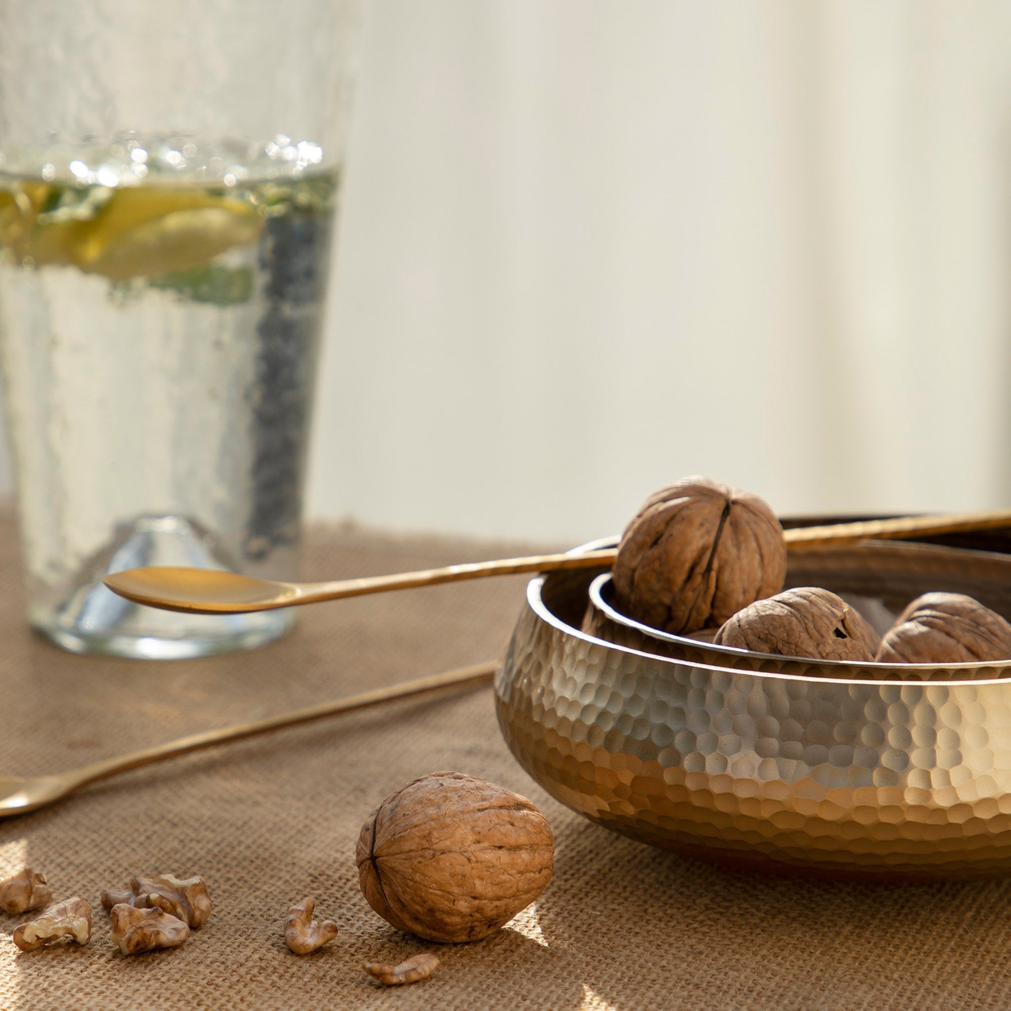 Bowl of walnuts with a glass of water and spoon on a textured surface