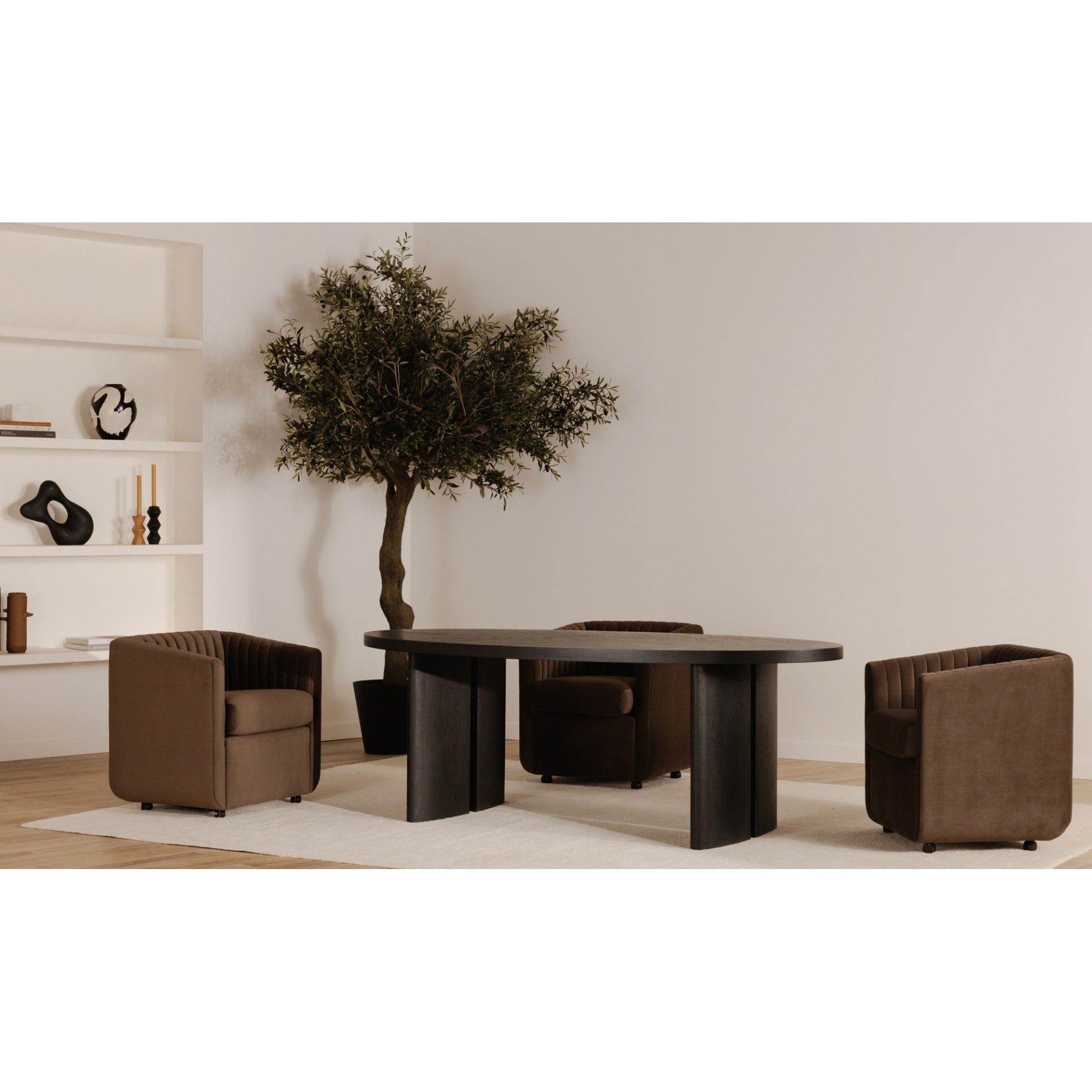 Modern living room with a dark wooden table and two brown armchairs, featuring a plant and shelves in the background.