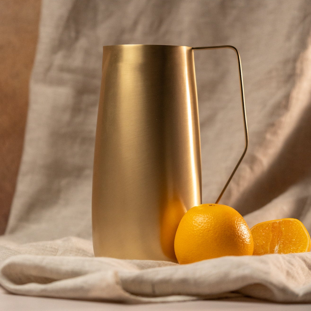 Gold pitcher with oranges on a textured fabric background