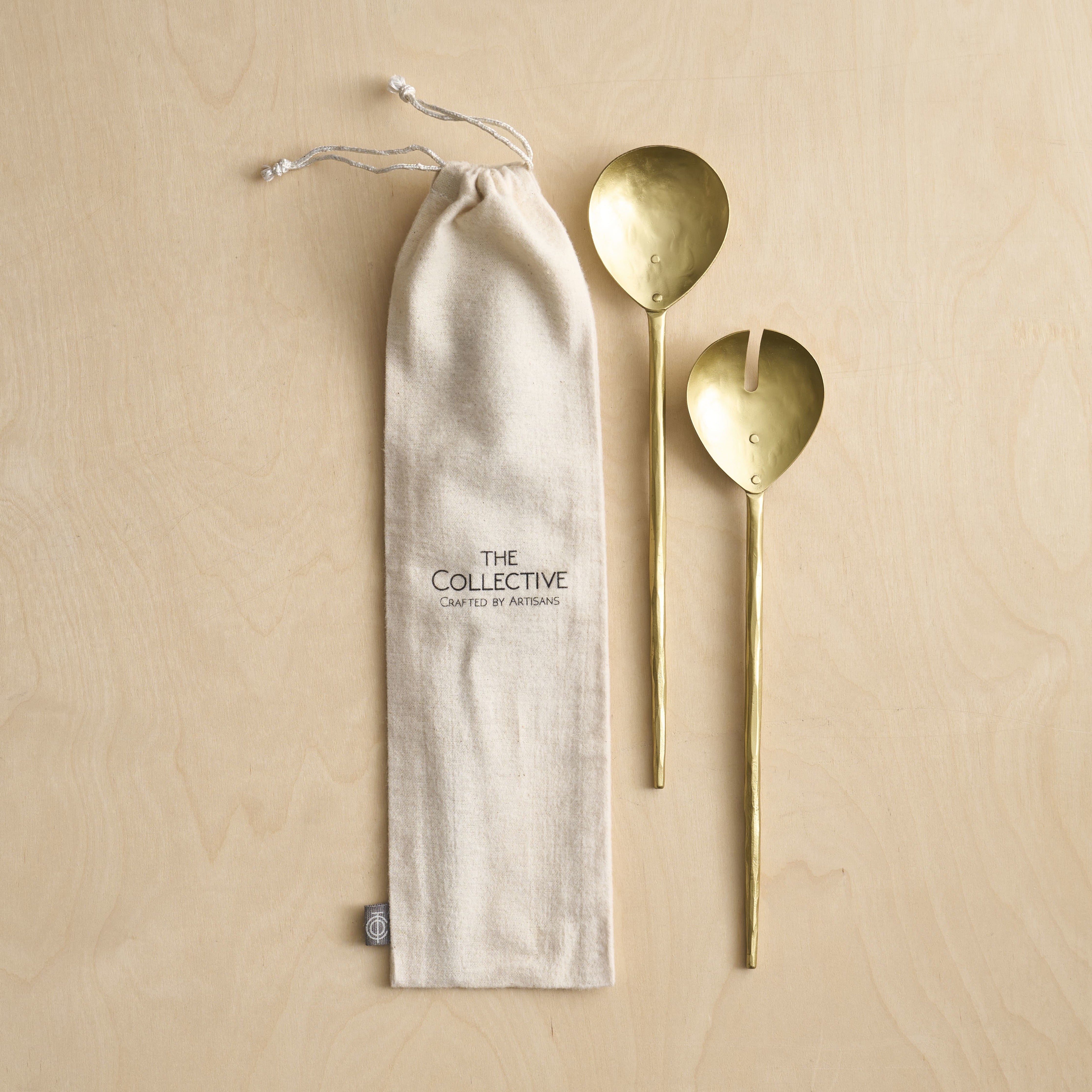 Two gold spoons next to a beige drawstring bag with 'The Collective' branding on a beige background.