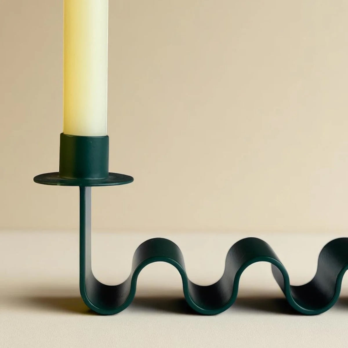 Wavy green candle holder with a candle on a beige background