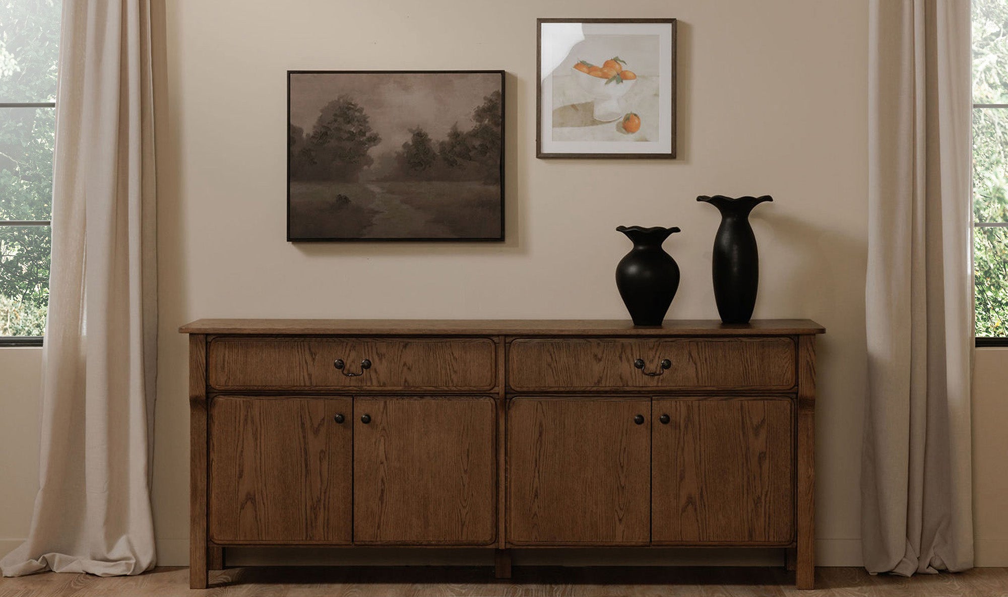 Wooden sideboard with two black vases and framed artwork on a wall.