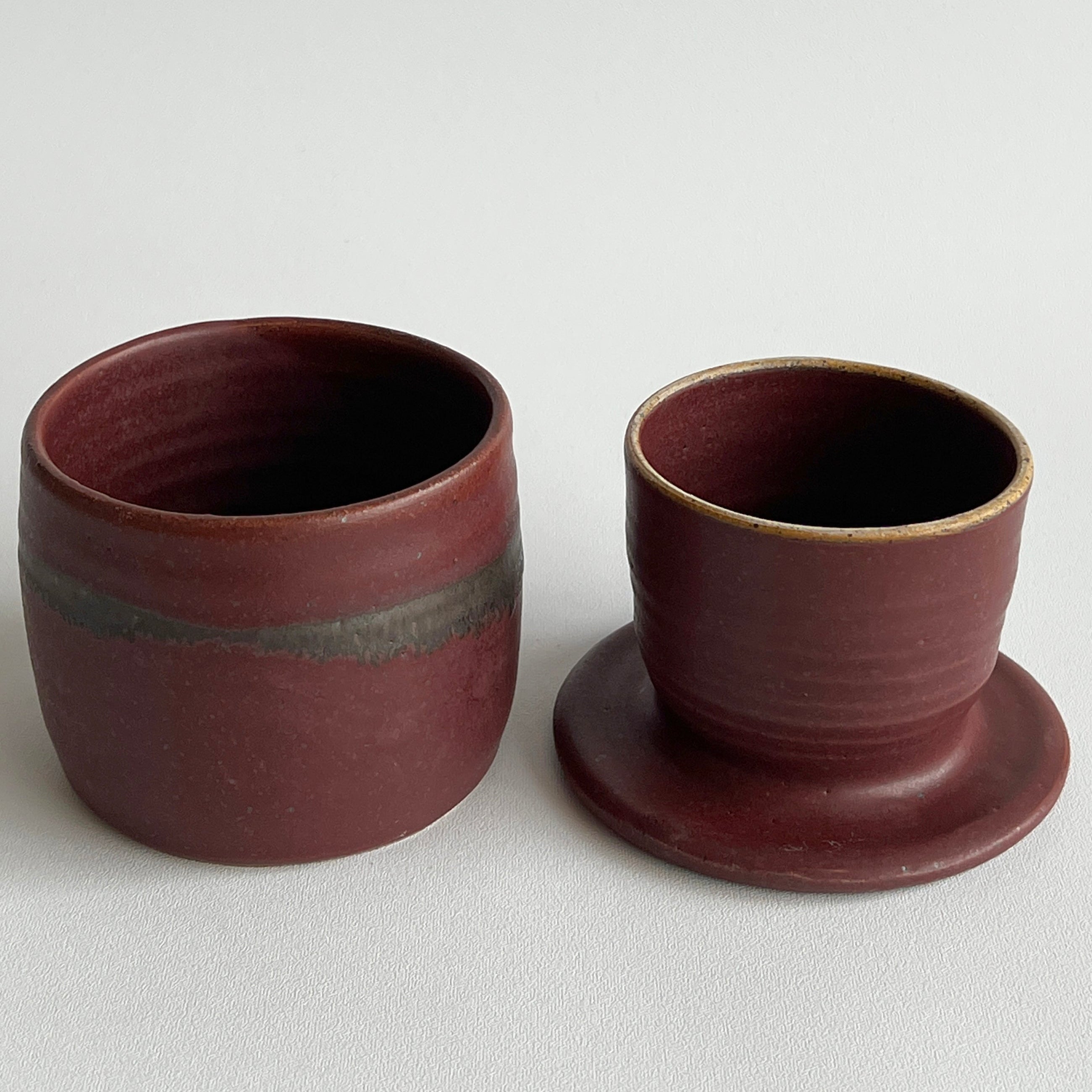 Two ceramic cups with a dark red brown glaze on a light gray background