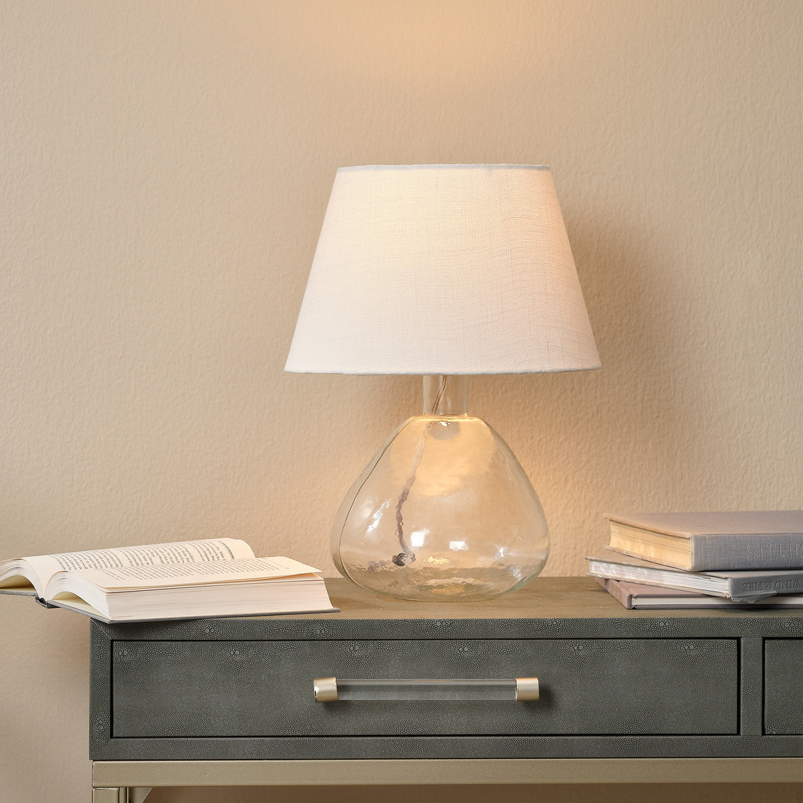 Table lamp with a glass base on a wooden surface against a beige wall