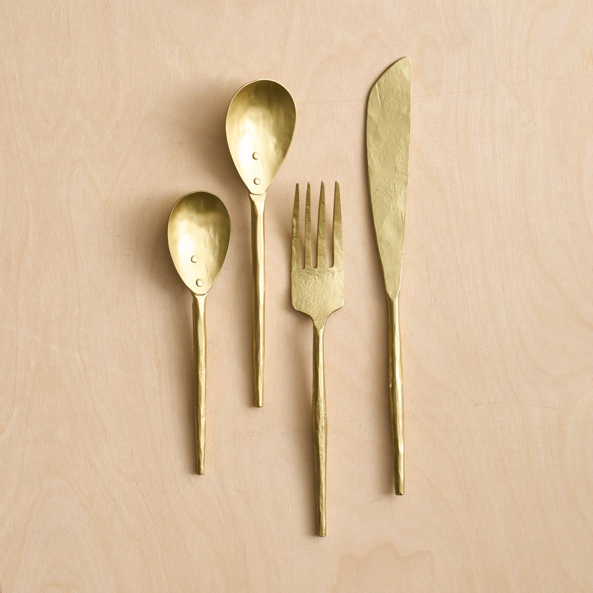 Set of gold flatware including a knife, fork, and two spoons on a beige background