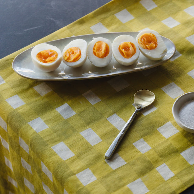 Sliced hard-boiled eggs on a plate with a spoon on a yellow checkered table runner.