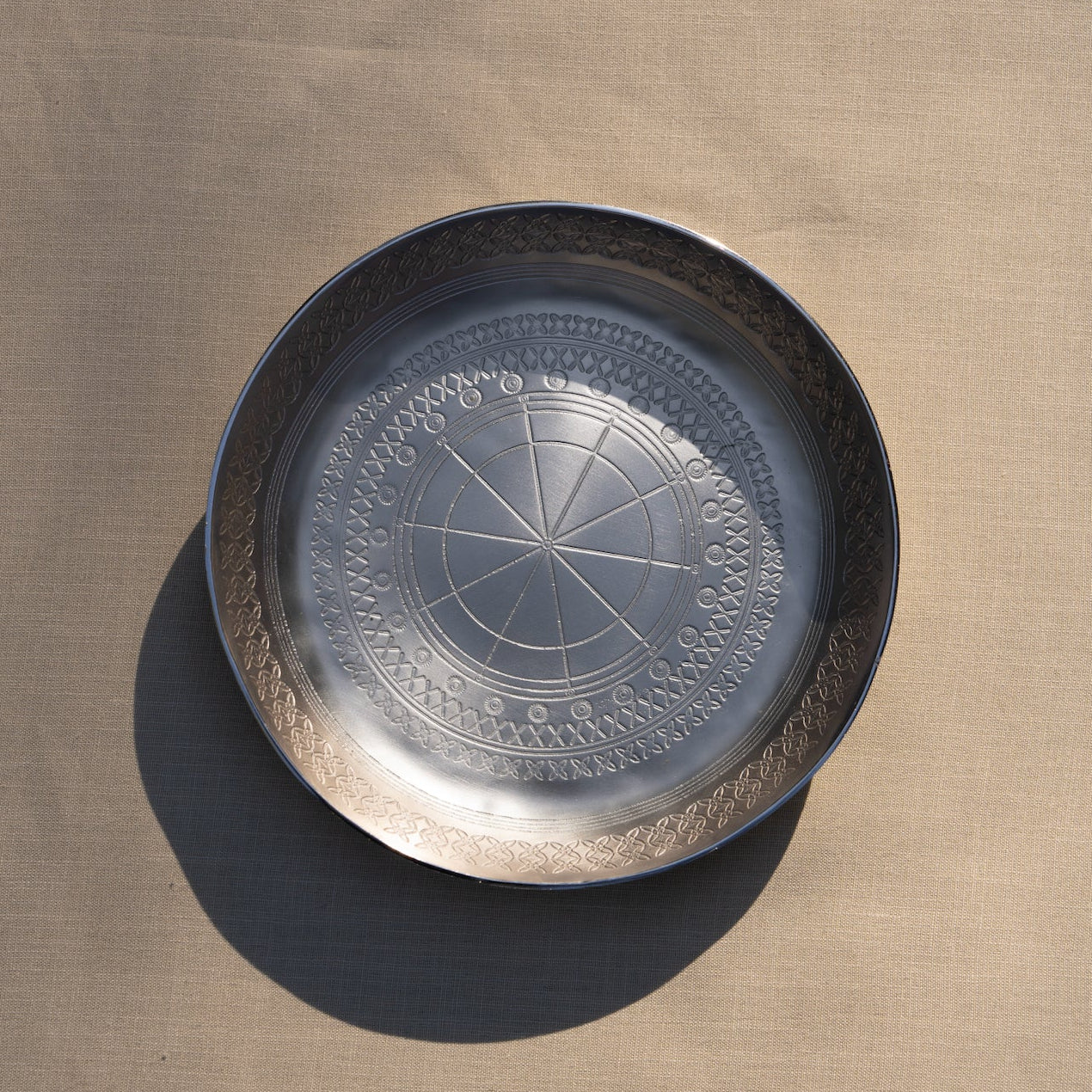 Decorative metal tray with intricate design on a beige surface