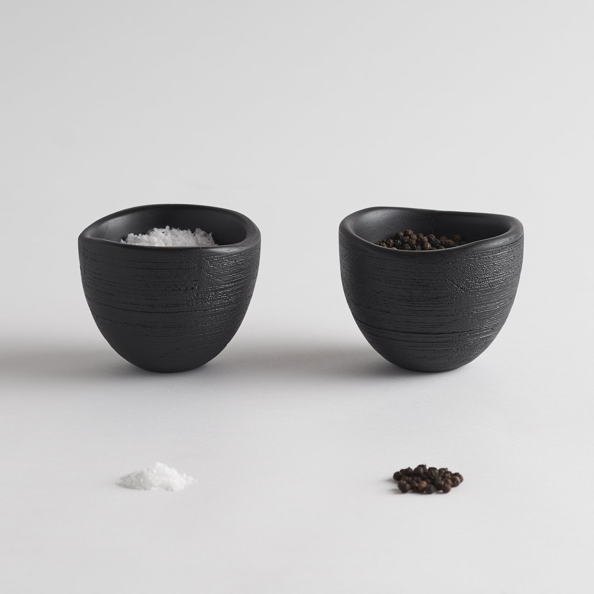 Two black wooden bowls filled with salt and pepper on a light gray background