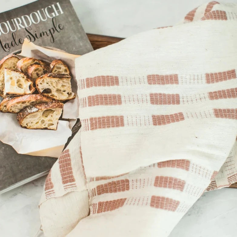 Loaves of bread on a wooden board with a patterned towel and 'Bread Made Simple' book.