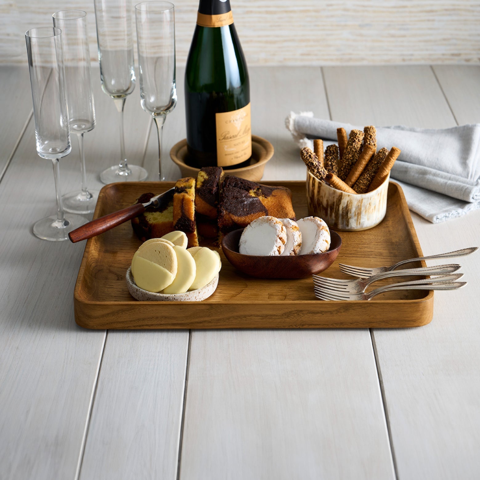 Wooden tray with cheese, crackers, and a bottle of wine on a light wooden surface.