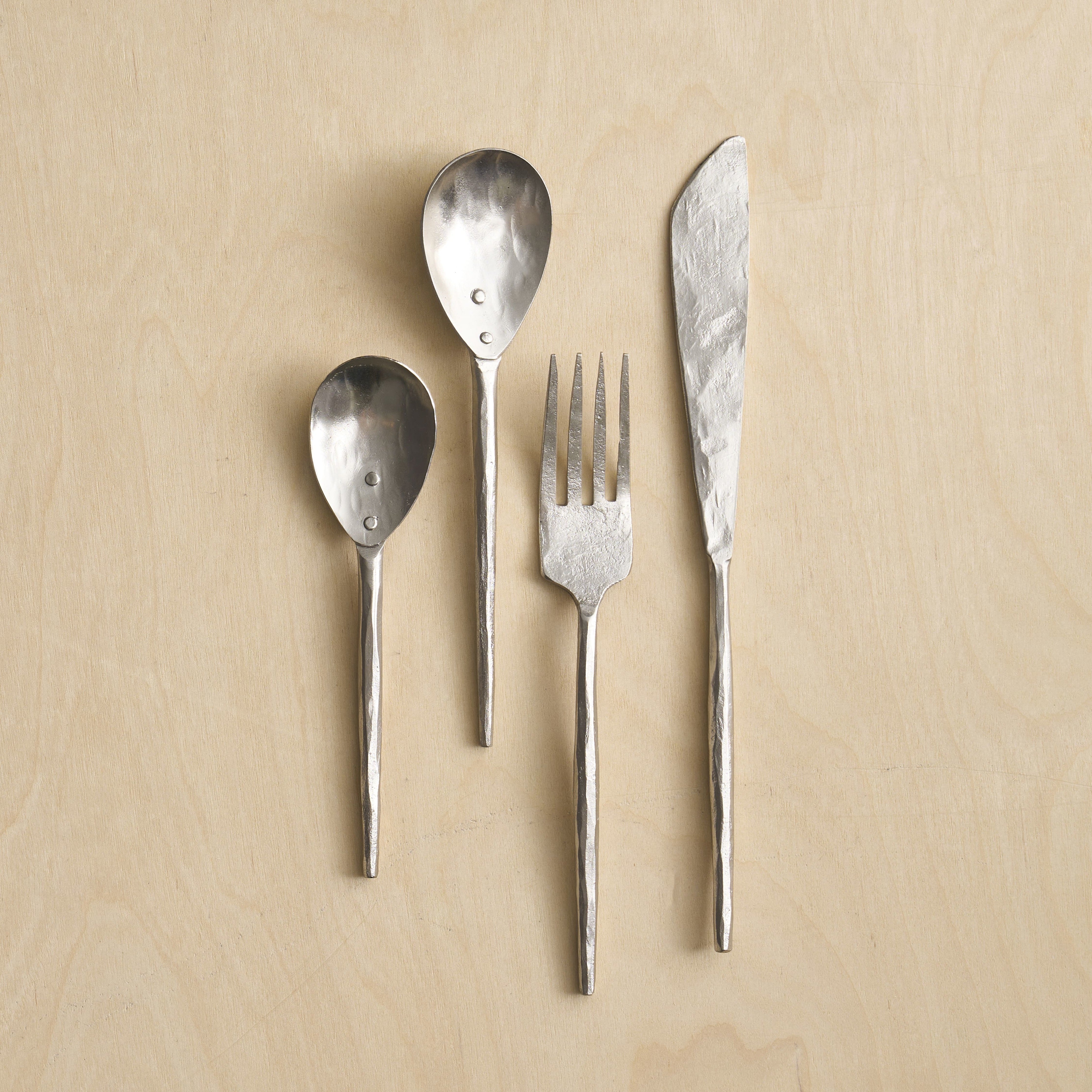 Set of silver cutlery including a knife, fork, and two spoons on a beige background