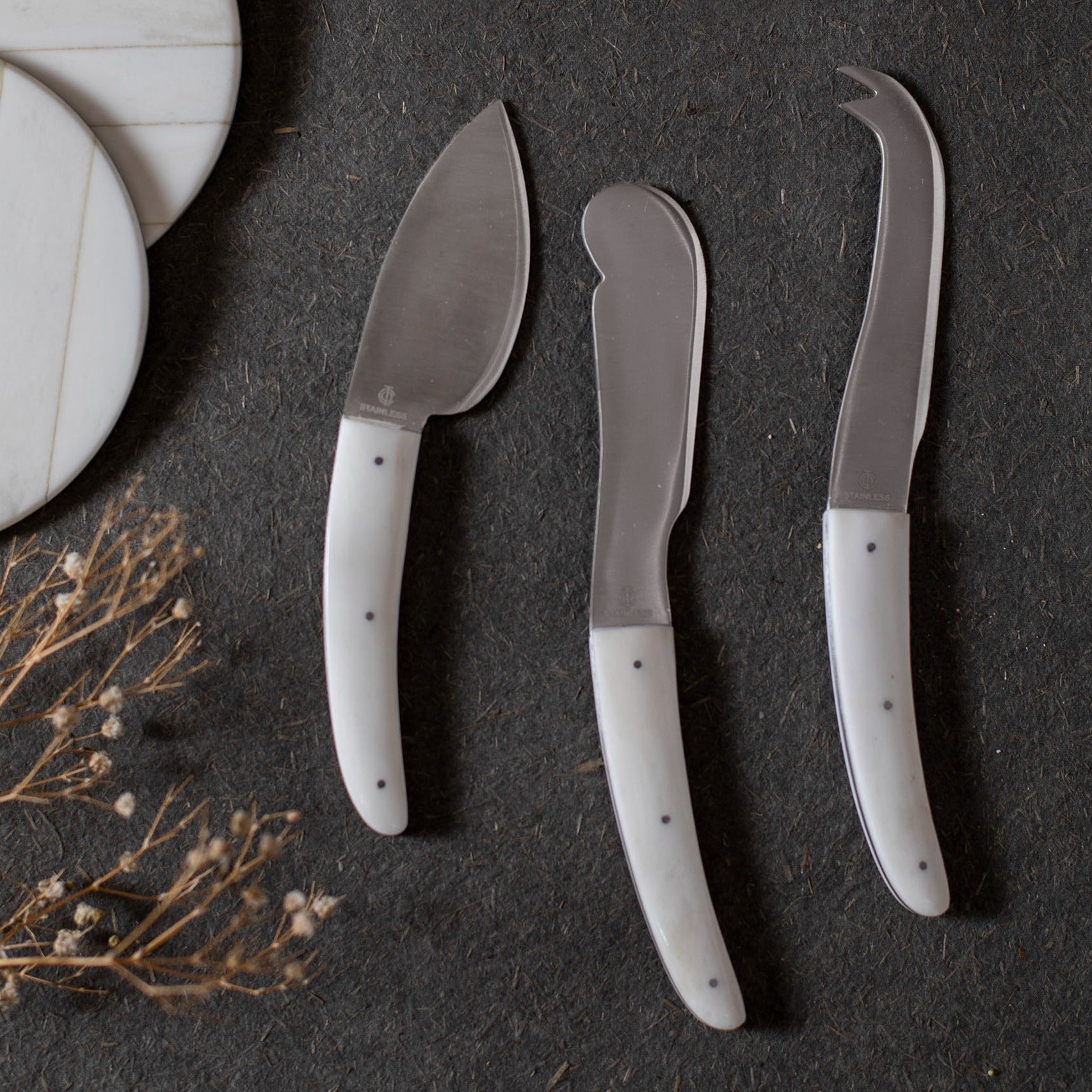 Three cheese knives with white handles on a dark surface.
