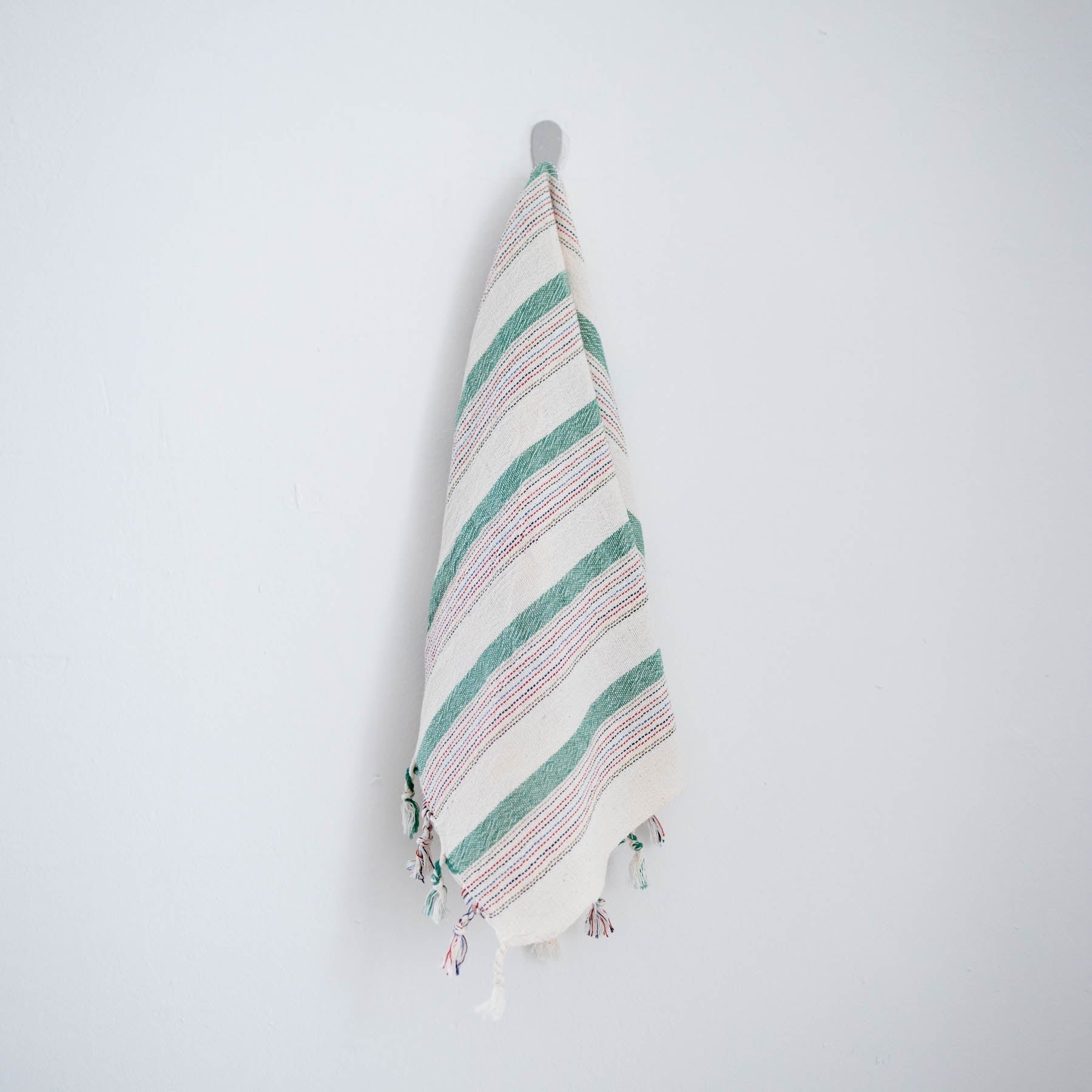 Green Striped towel with tassels hanging on a white wall