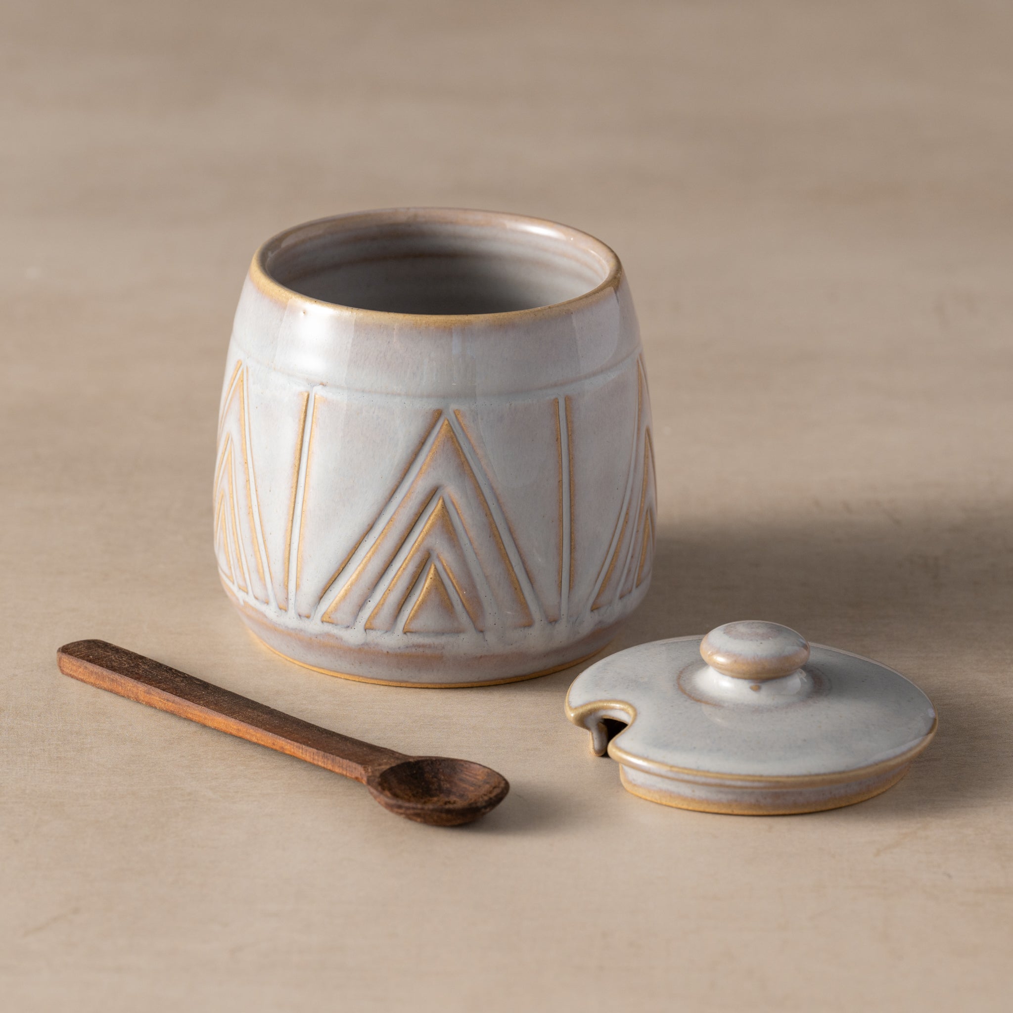 Ceramic container with lid and wooden spoon on a beige background