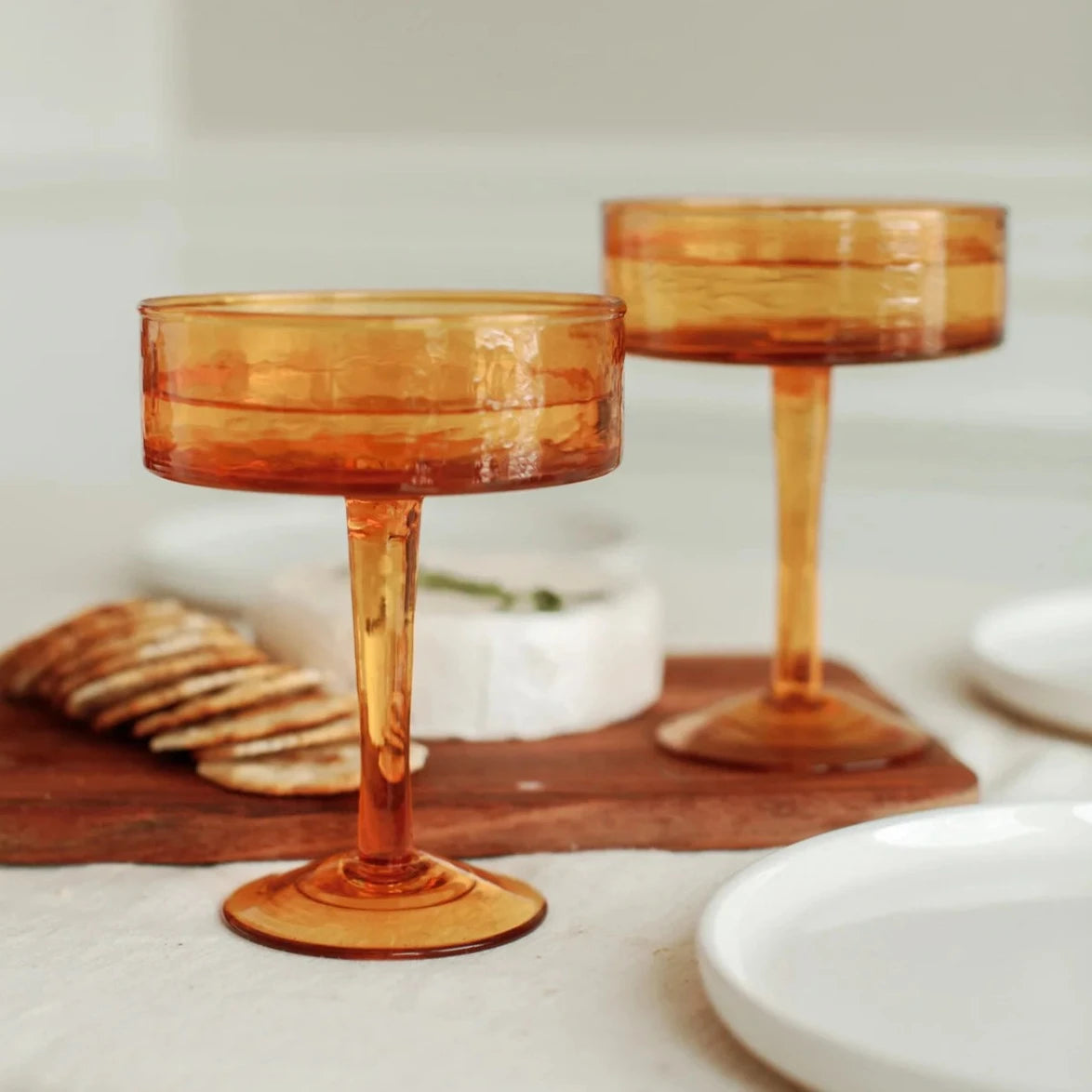 Two amber-colored cocktail glasses on a wooden board with a blurred background