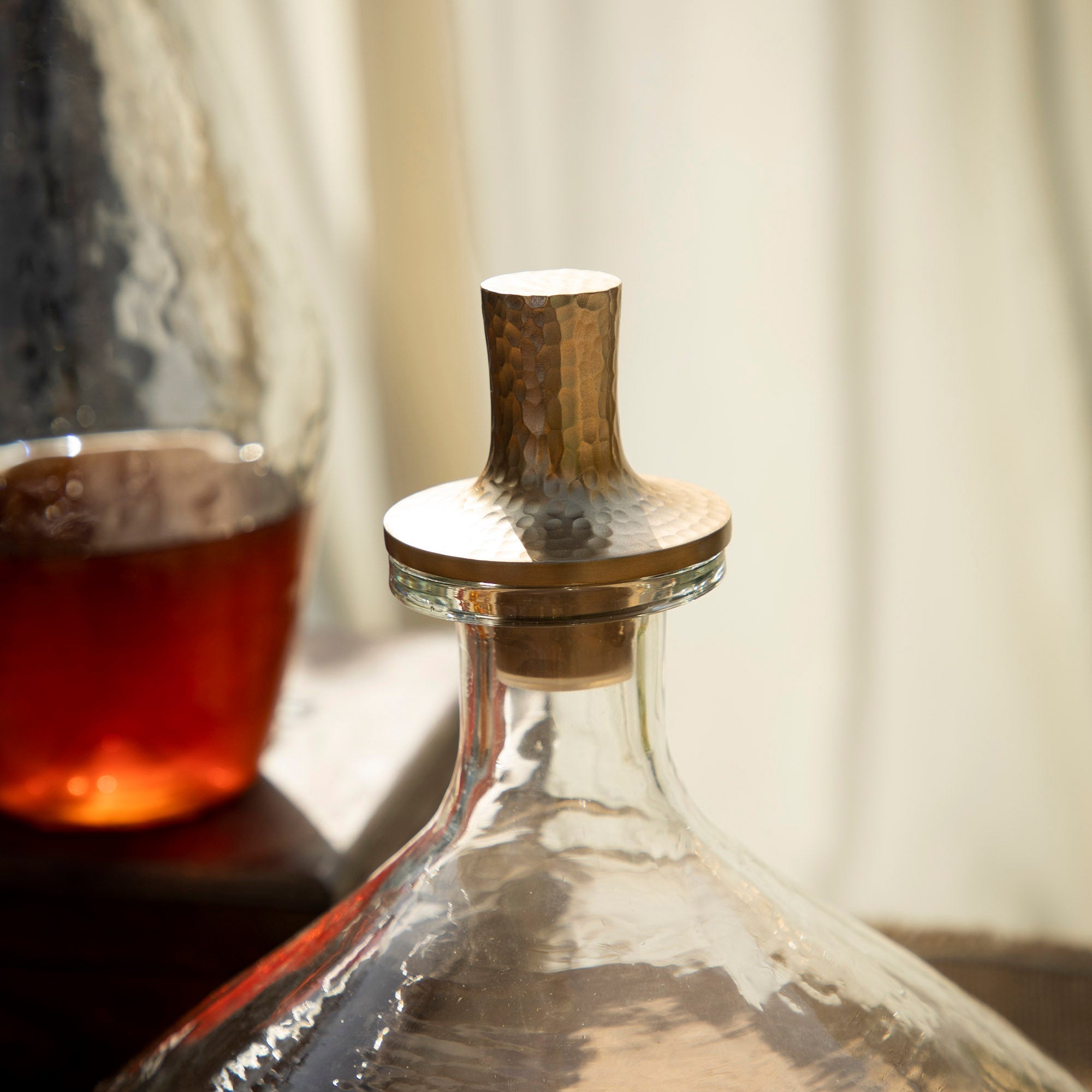 Clear glass decanter with wooden stopper next to a glass of amber liquid on a neutral background