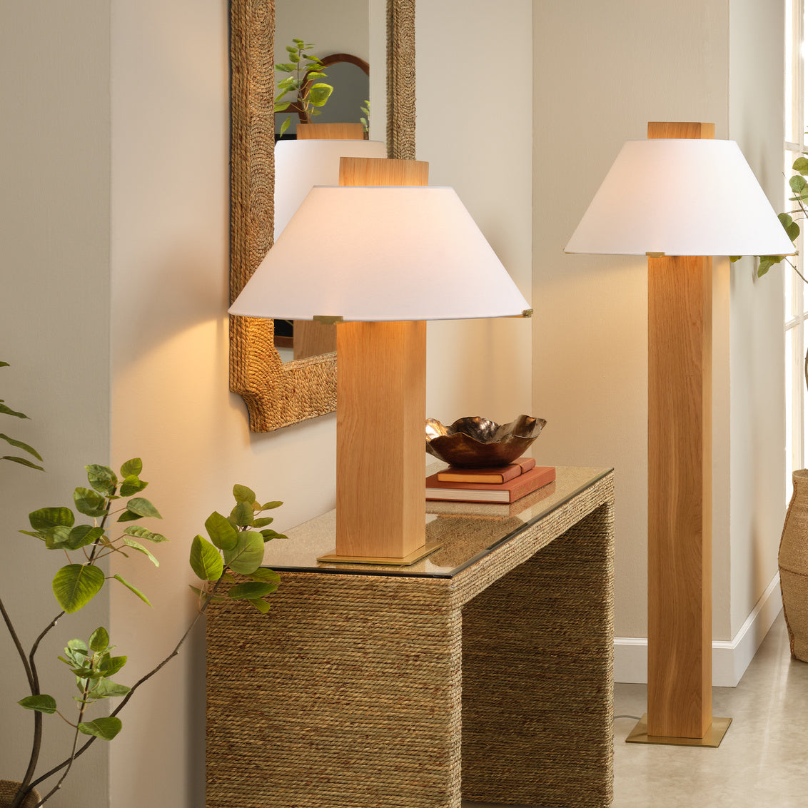 Two wooden table lamps on a textured side table with a mirror and books in the background.