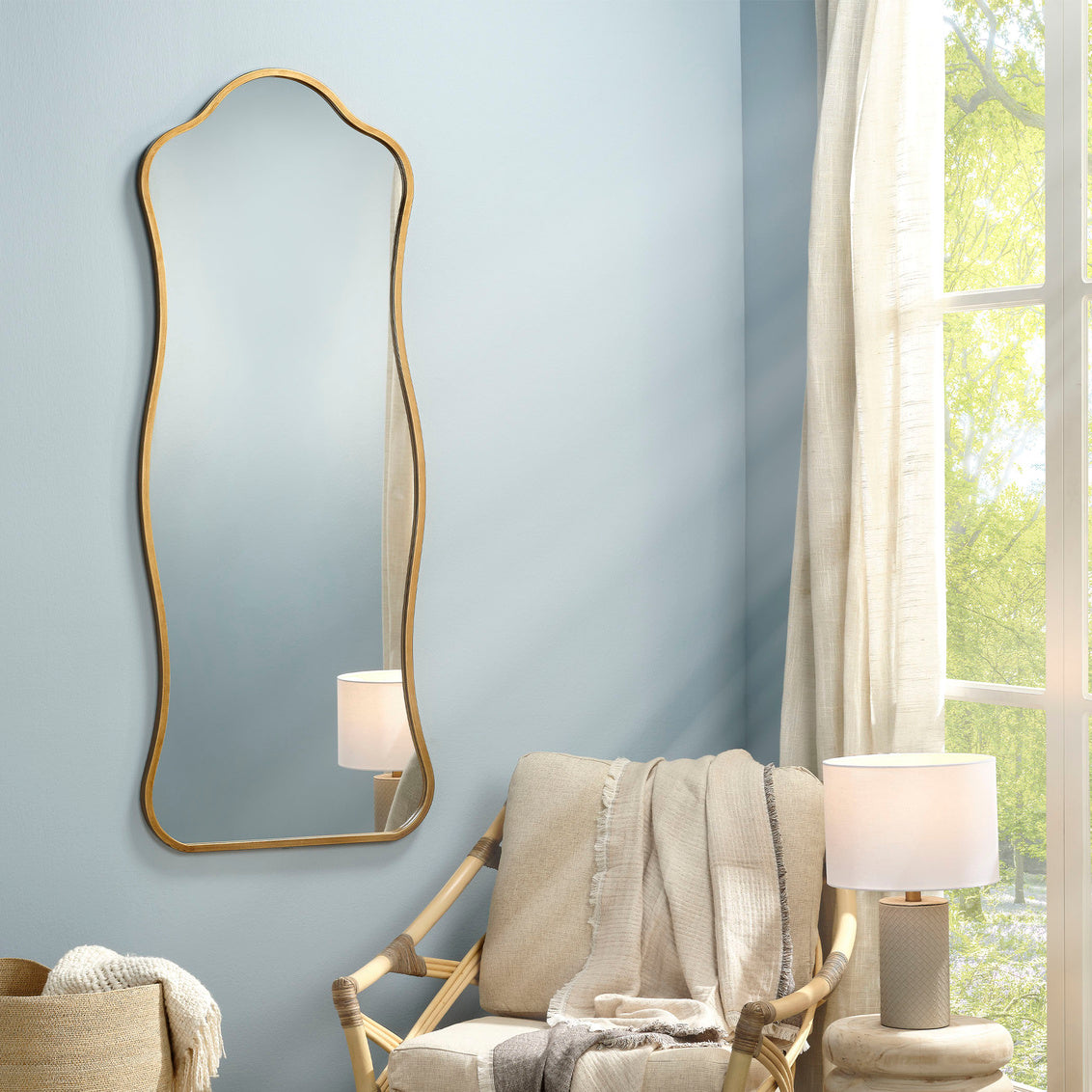 Decorative mirror on a wall with a chair and lamp in a room with a window.