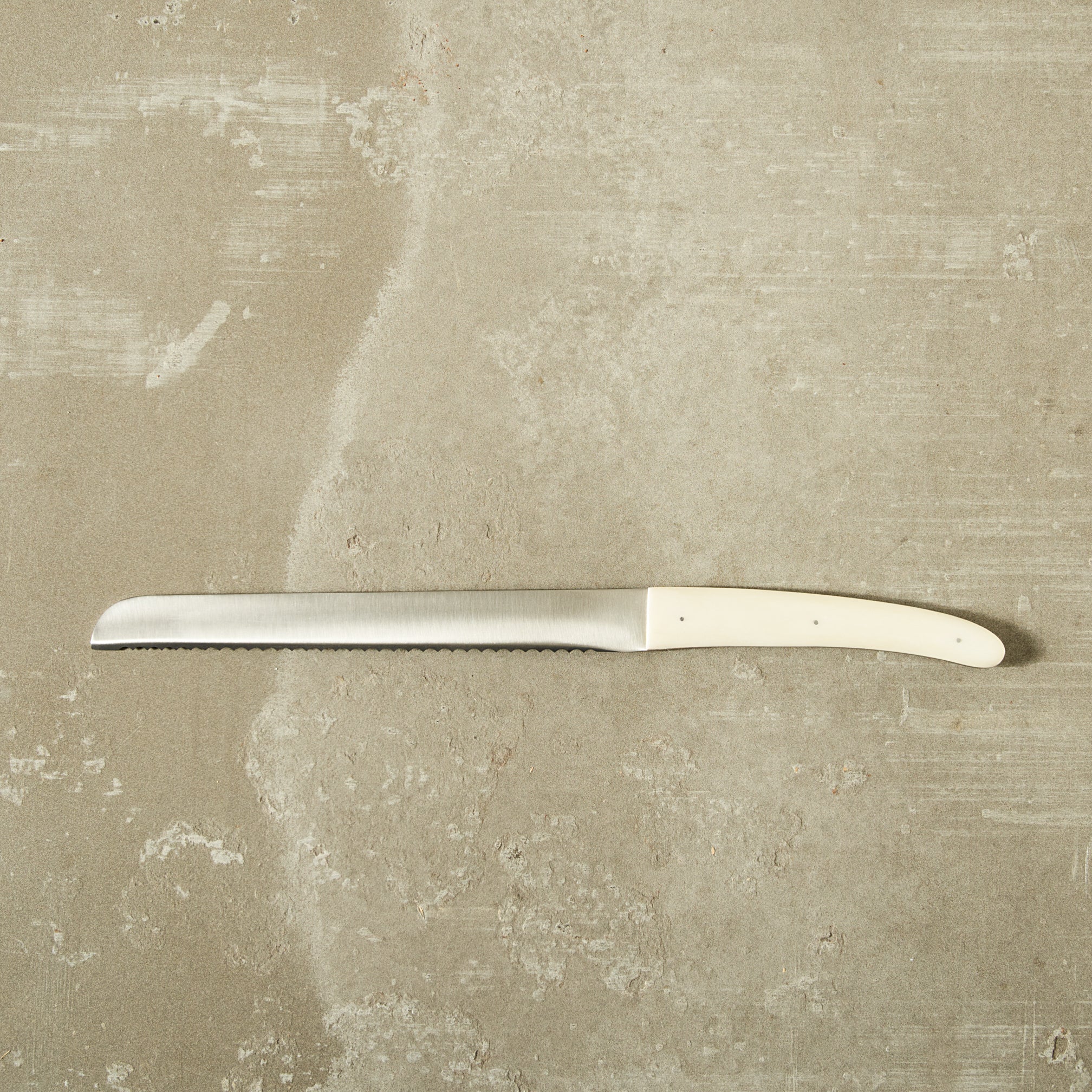 Bread knife with a white bone handle on a textured beige surface