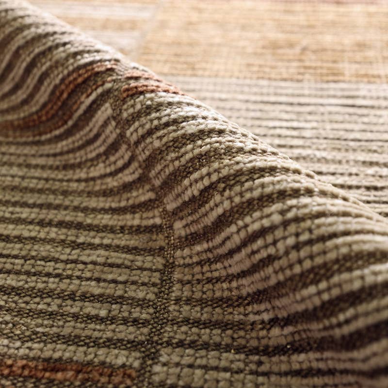 Close-up of a woven rug with a textured striped pattern in beige, brown, and muted rust tones.