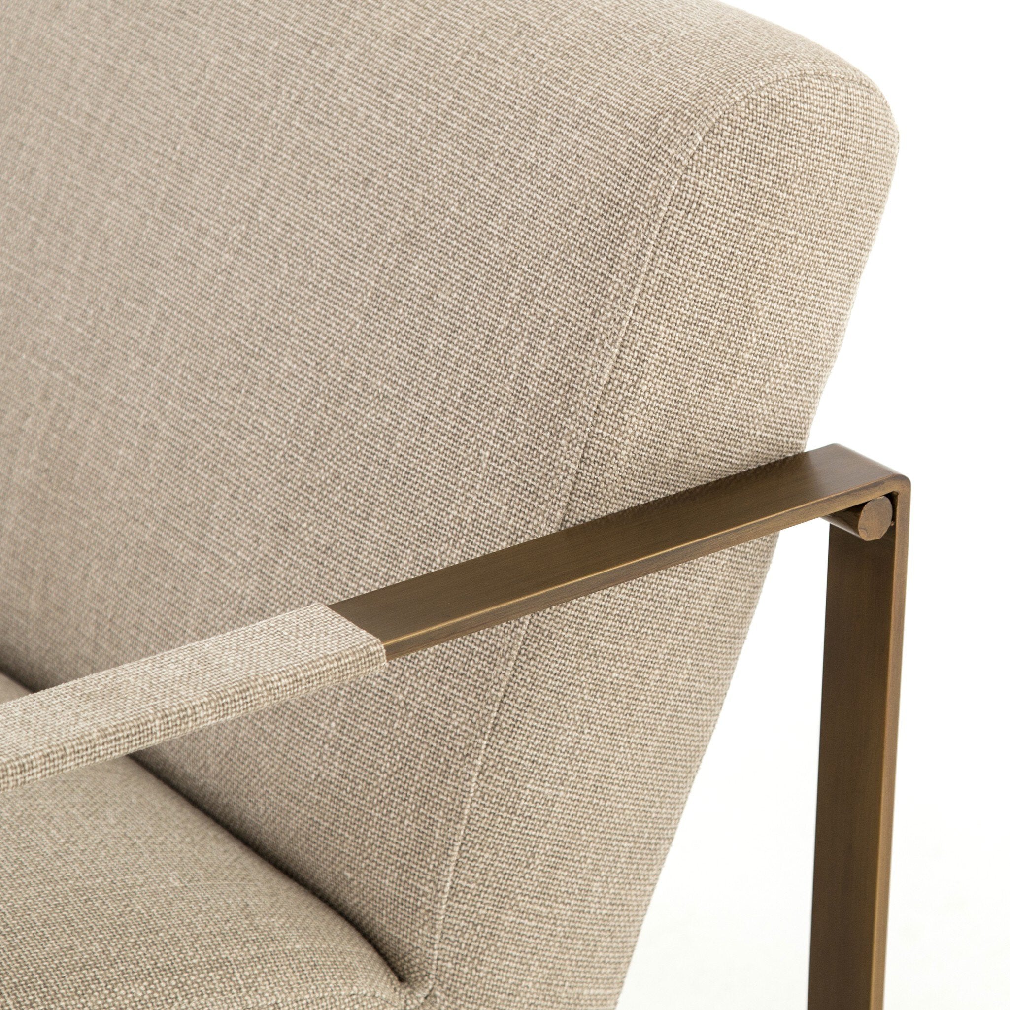 Close-up of a beige upholstered chair with a bronze armrest and leg.