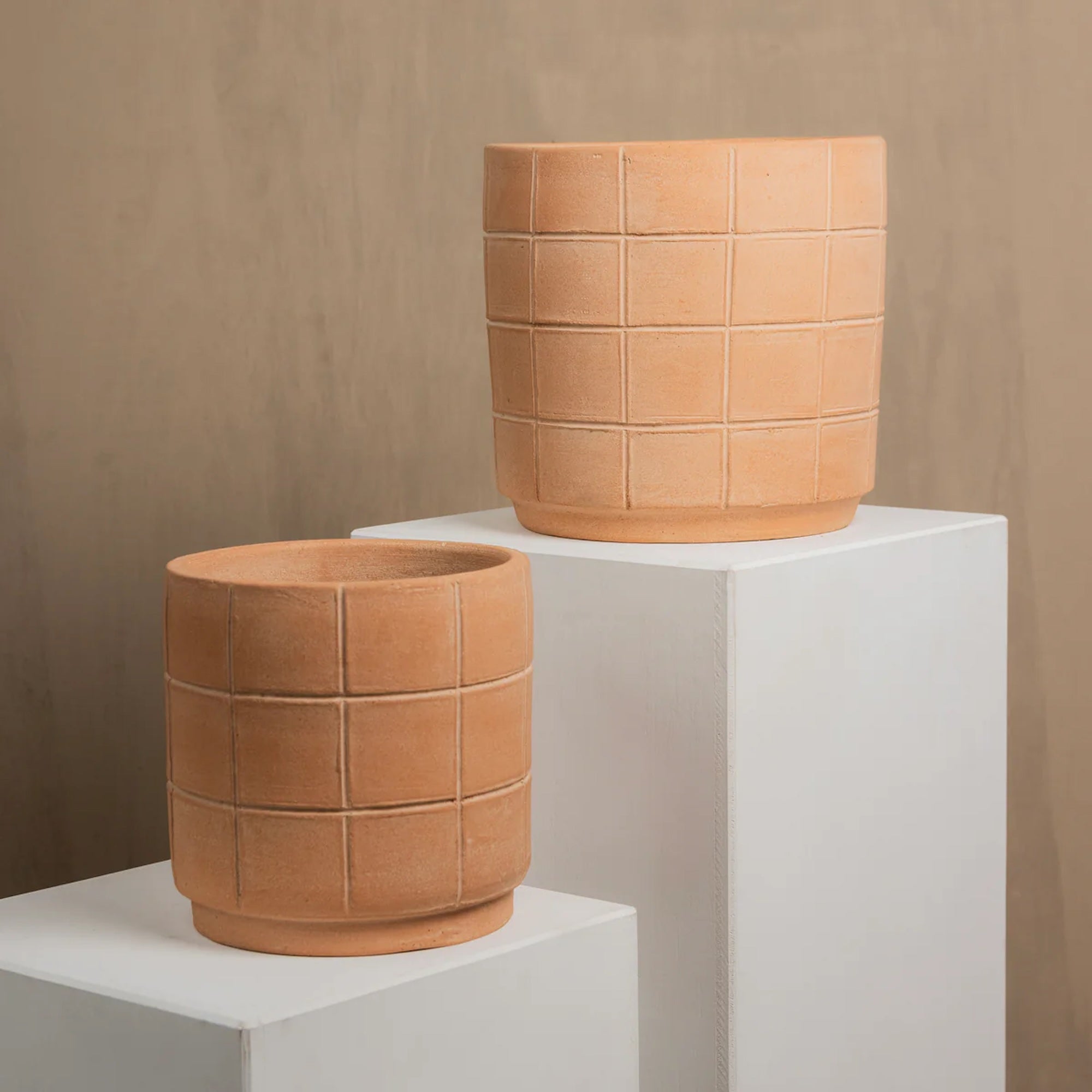 Two terracotta pots with a geometric pattern on a white pedestal against a beige background