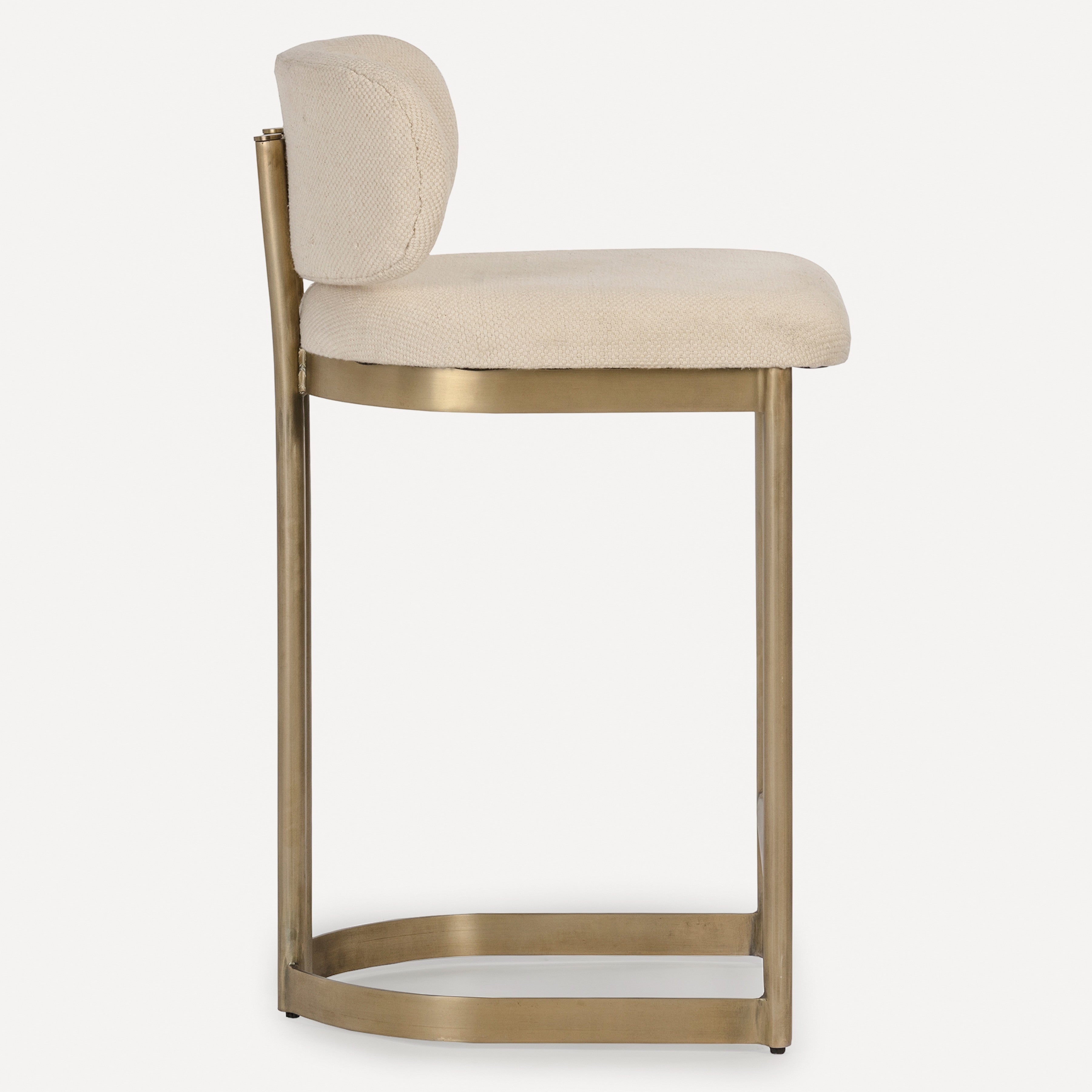 A modern bar stool with a curved, upholstered cream seat and backrest, supported by a sleek, brushed brass metal frame with a footrest, shown against a plain white background.