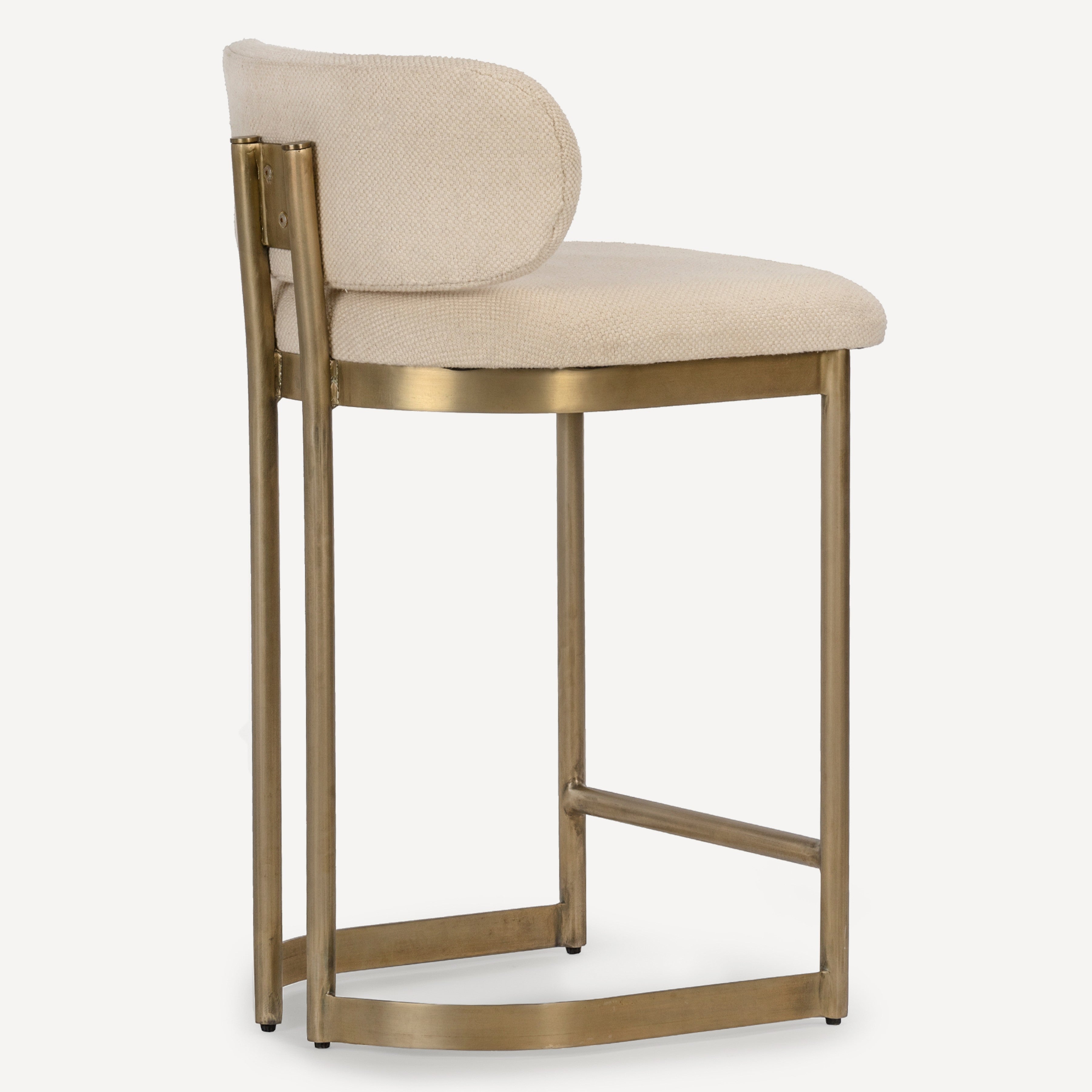 A modern bar stool with a curved upholstered backrest and seat in a light beige textured fabric, supported by a sleek curved brass-finished metal frame.