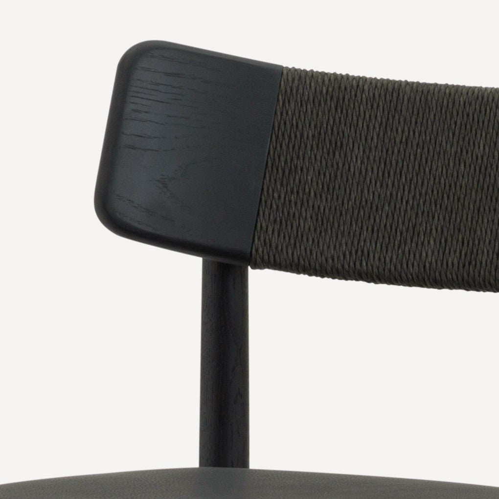 Close-up of a chair backrest showing a dark wood frame, a black upholstered section, and a dark gray woven rope back, set against a plain off-white background.