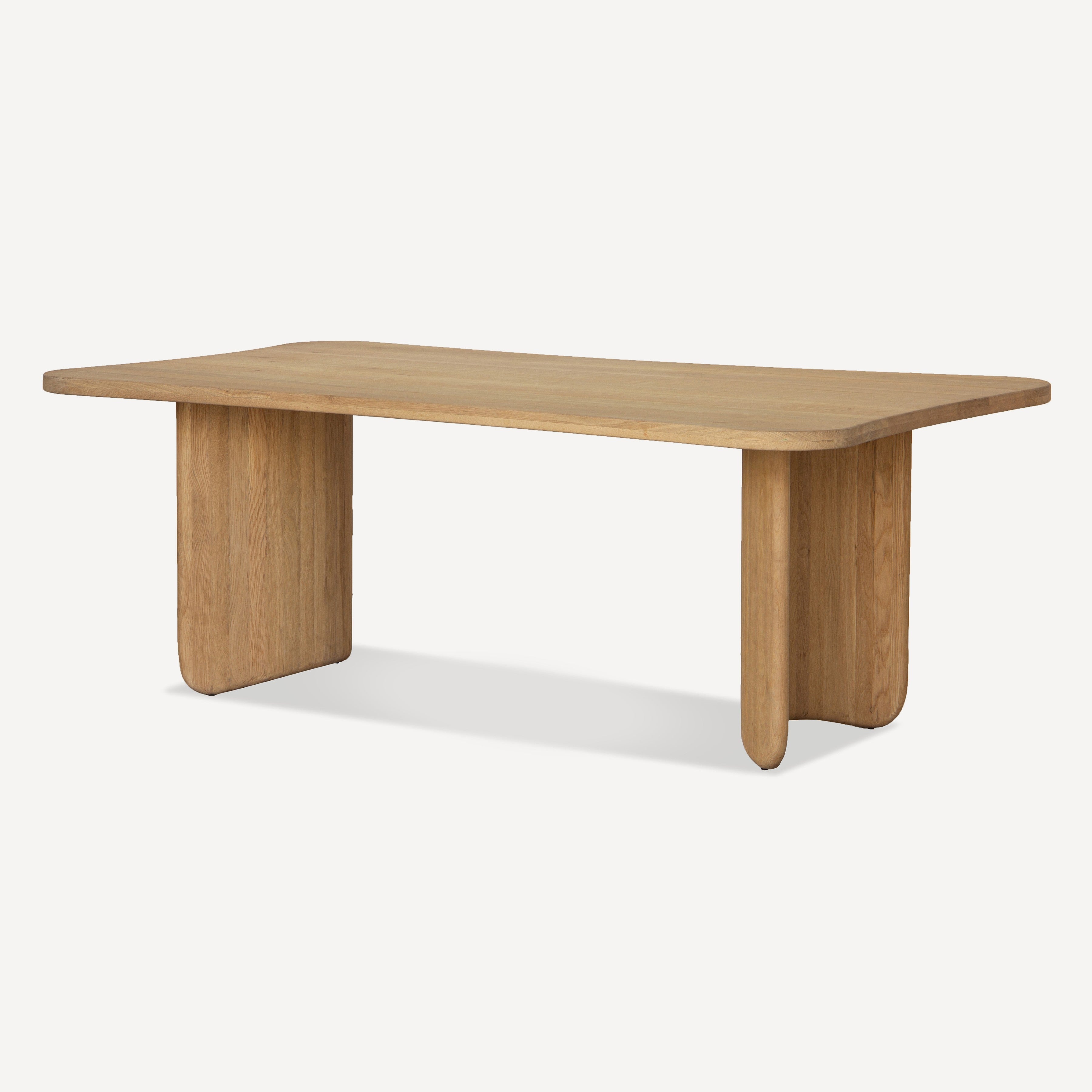 A modern rectangular wooden table with rounded corners and thick block-style legs, shown on a clean off-white background.
