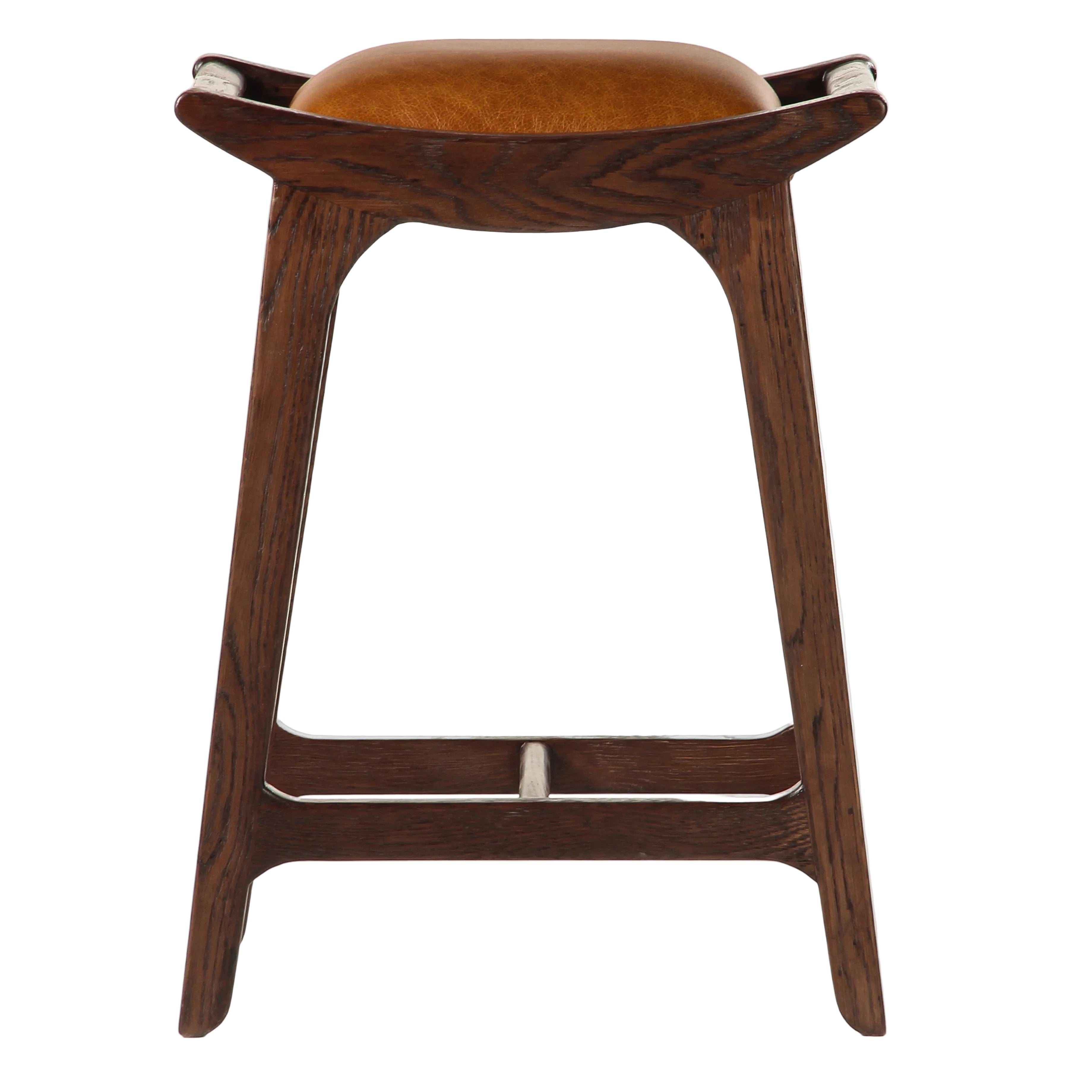 A mid-century modern wooden bar stool with a curved dark brown wood frame, a brown leather seat cushion, and small silver metal accents on the armrests and legs, shown against a plain white background.